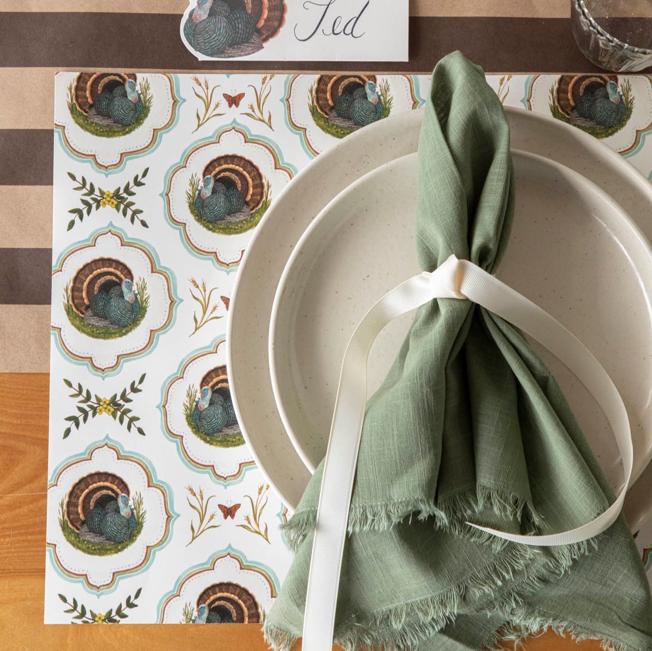 Top view of the Heritage Turkey Meadow placemat with dinner plates and a napkin on top.