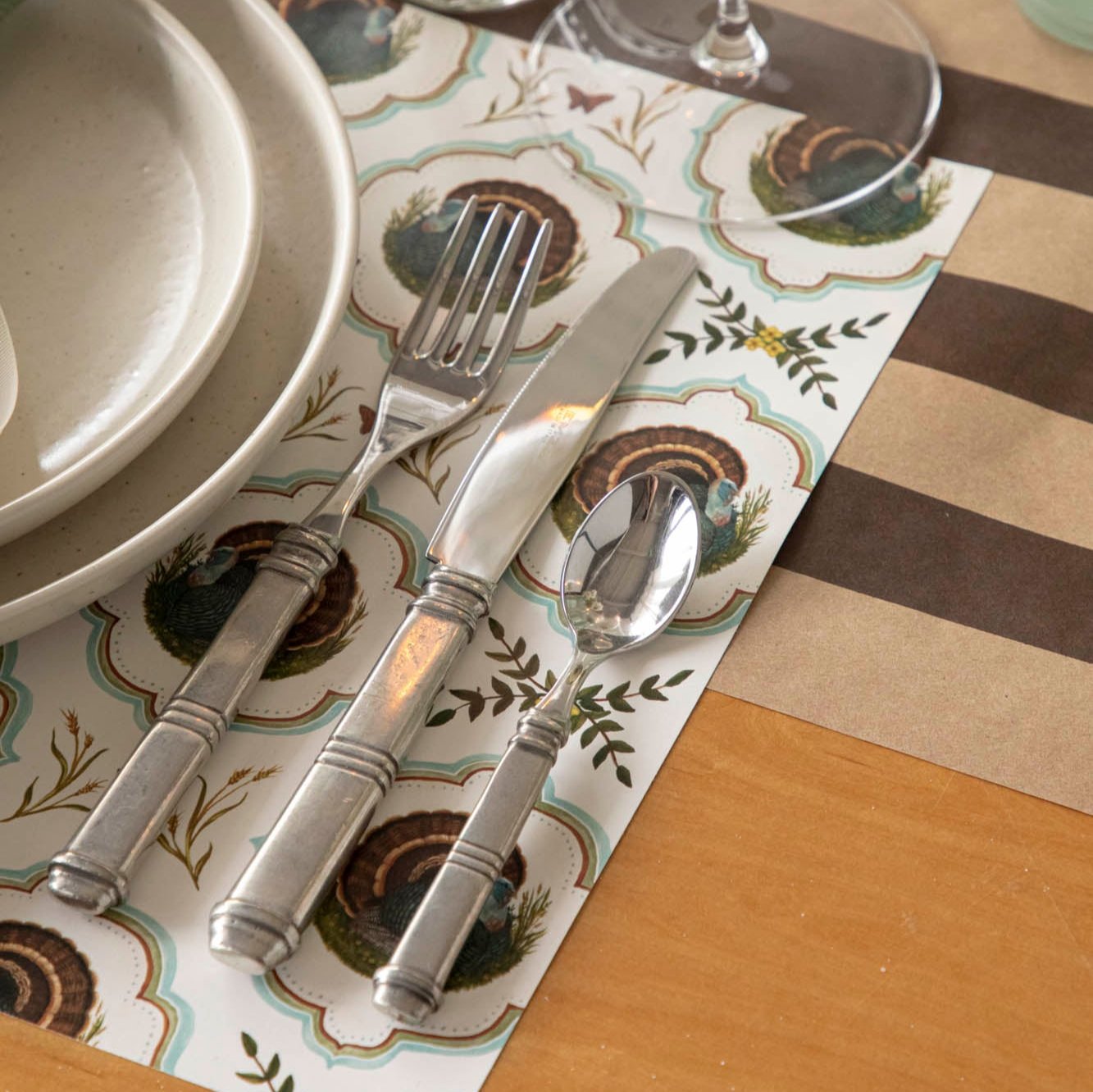 Close up view of the Heritage Turkey Meadow Placemat with silverware and dinner plates on top.