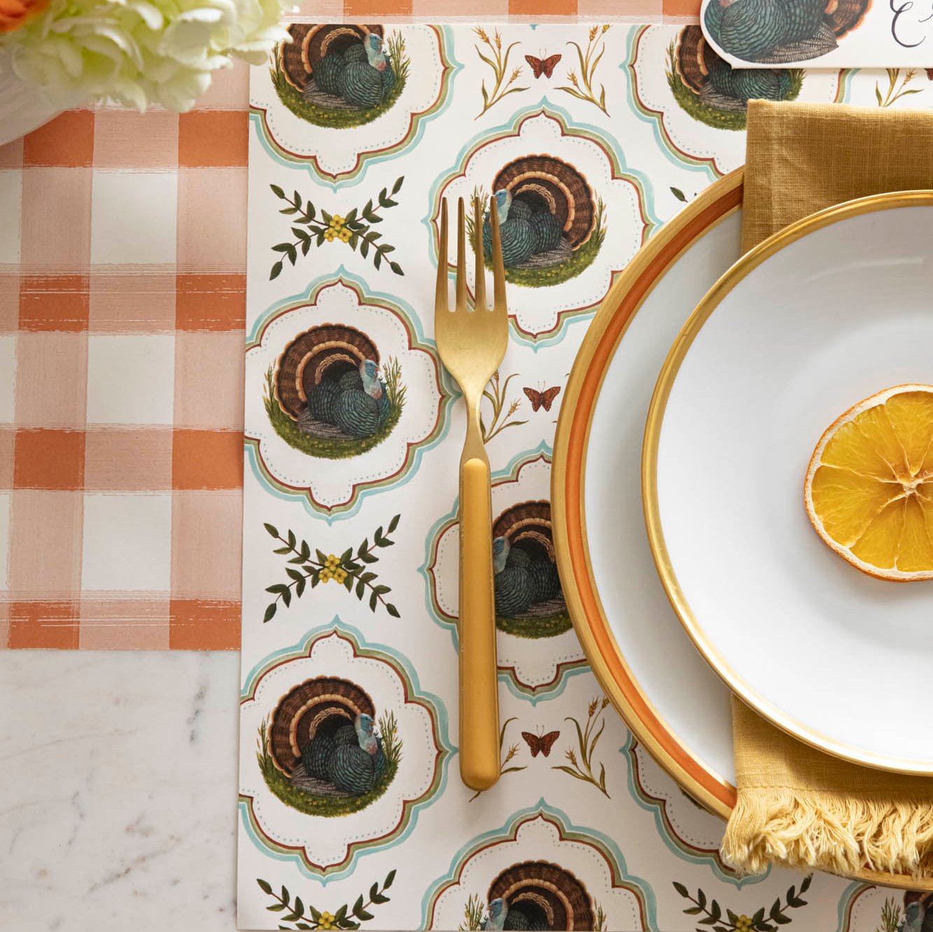 Heritage Turkey Meadow Placemat on an orange checked runner with dinnerware on top.