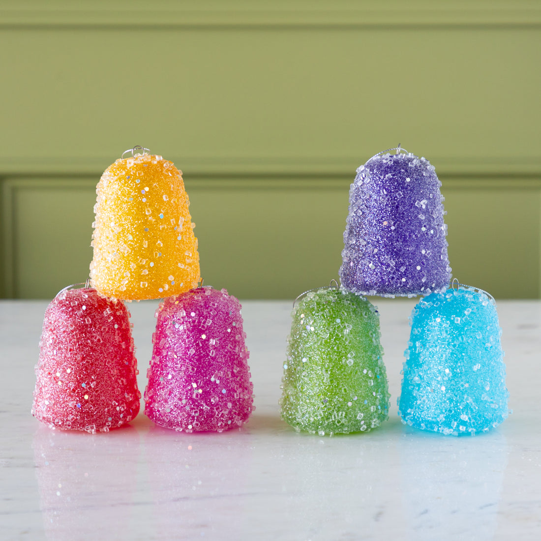 Colorful Glittered Gum Drop Ornaments stacked on a marble surface with a green background.