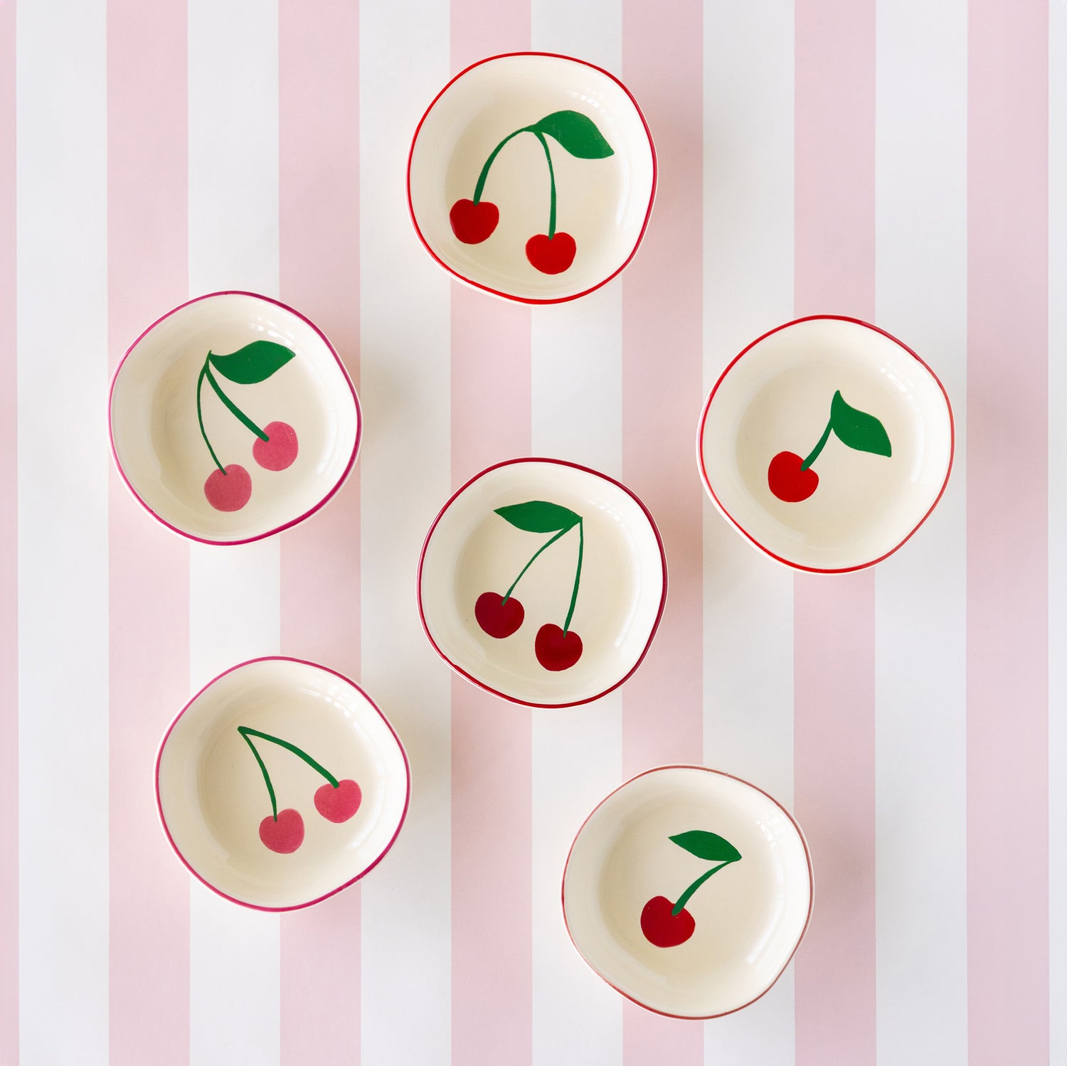 Six ceramic cherry pinch bowls with red rims and charming cherry illustrations inside, arranged on the Pink Classic Stripe Runner.