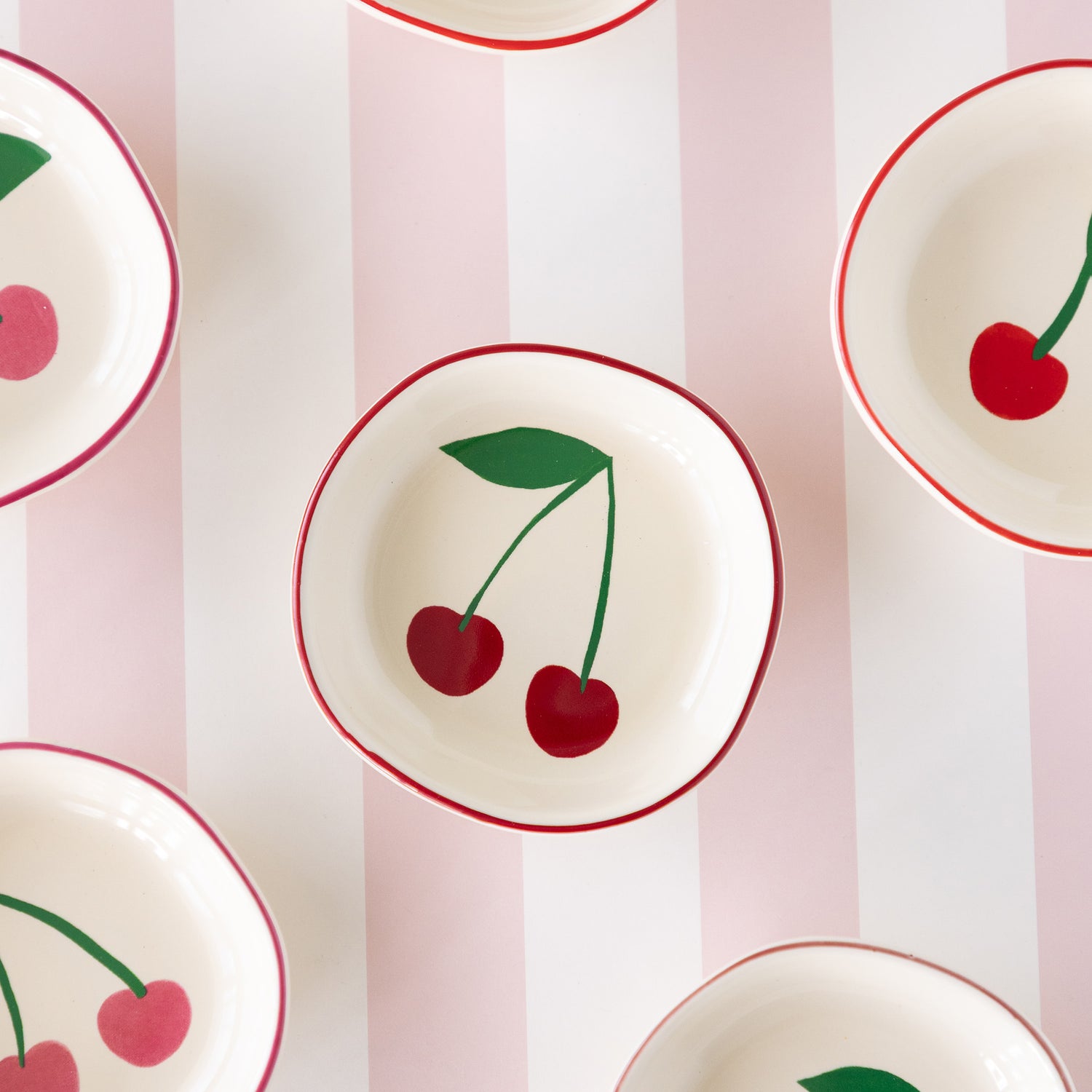 The Very Cherry pinch bowl featuring a white ceramic bowl with a red rim and a dark red cherry design inside.