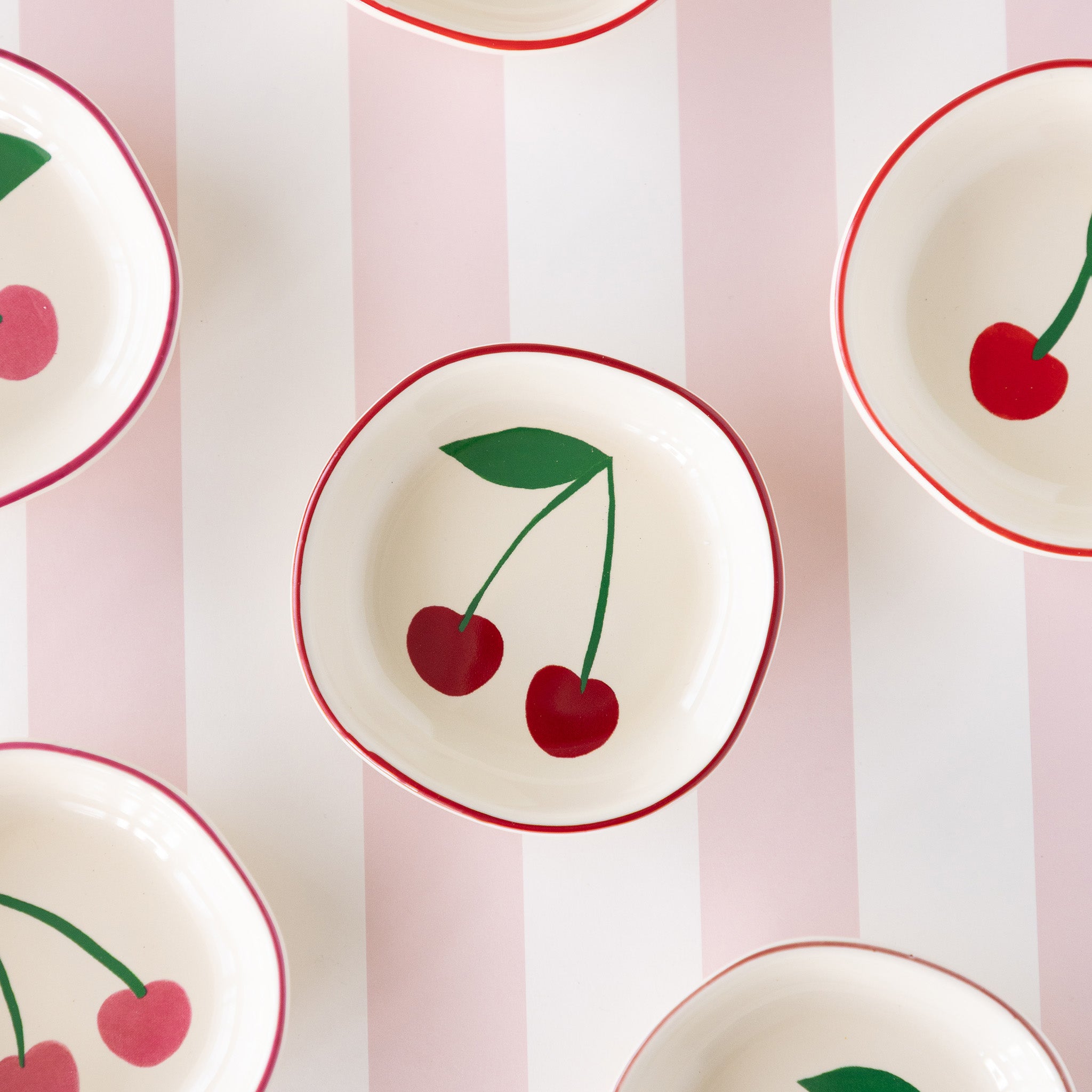 The Very Cherry pinch bowl featuring a white ceramic bowl with a red rim and a dark red cherry design inside.