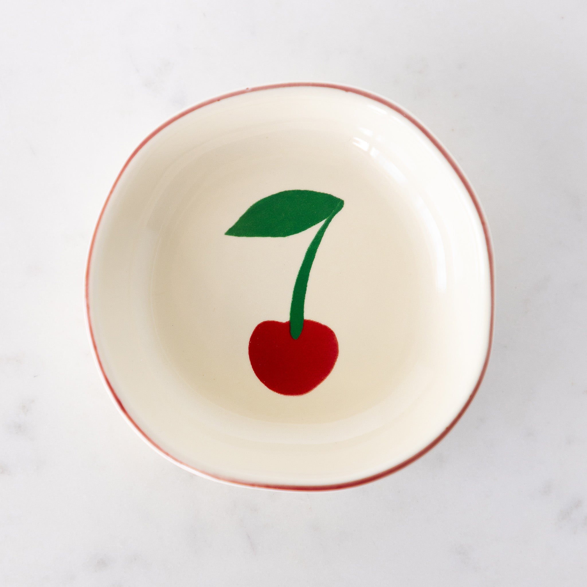 A white ceramic pinch bowl with a red rim features a painted red cherry with a green leaf.