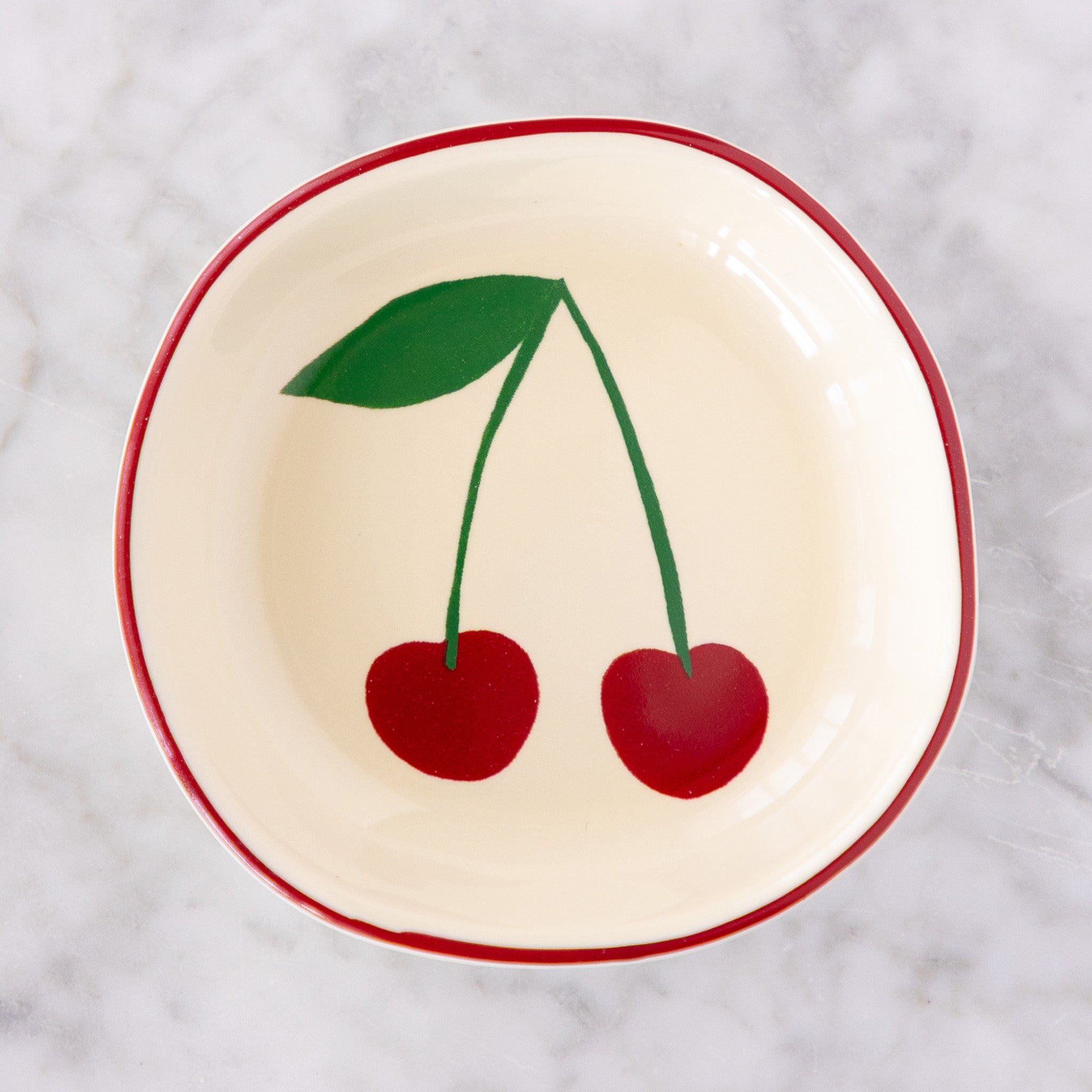 A white ceramic pinch bowl with a red rim features two painted red cherries with a green leaf.