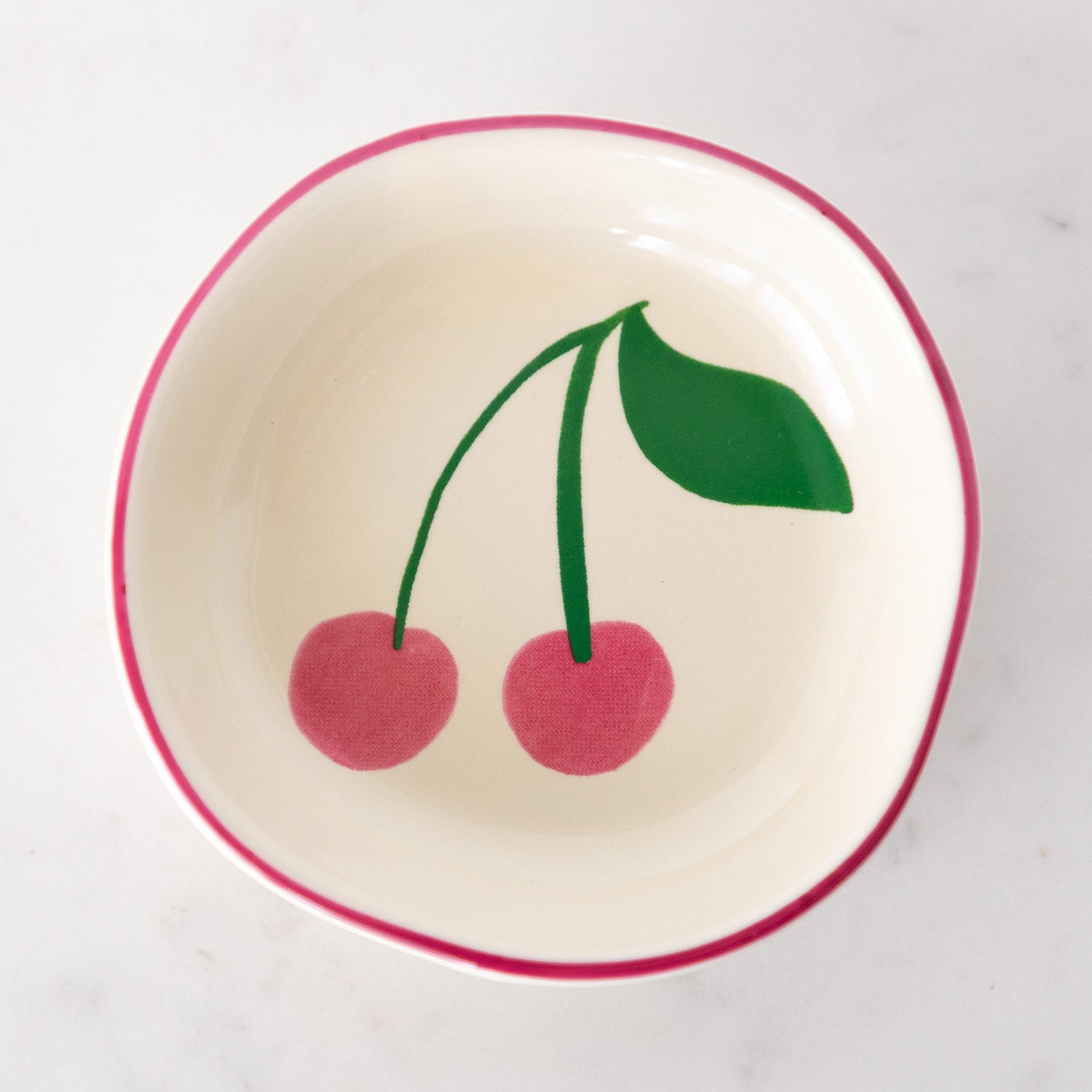 A white ceramic pinch bowl with a pink rim features two painted pink cherries with a green leaf.