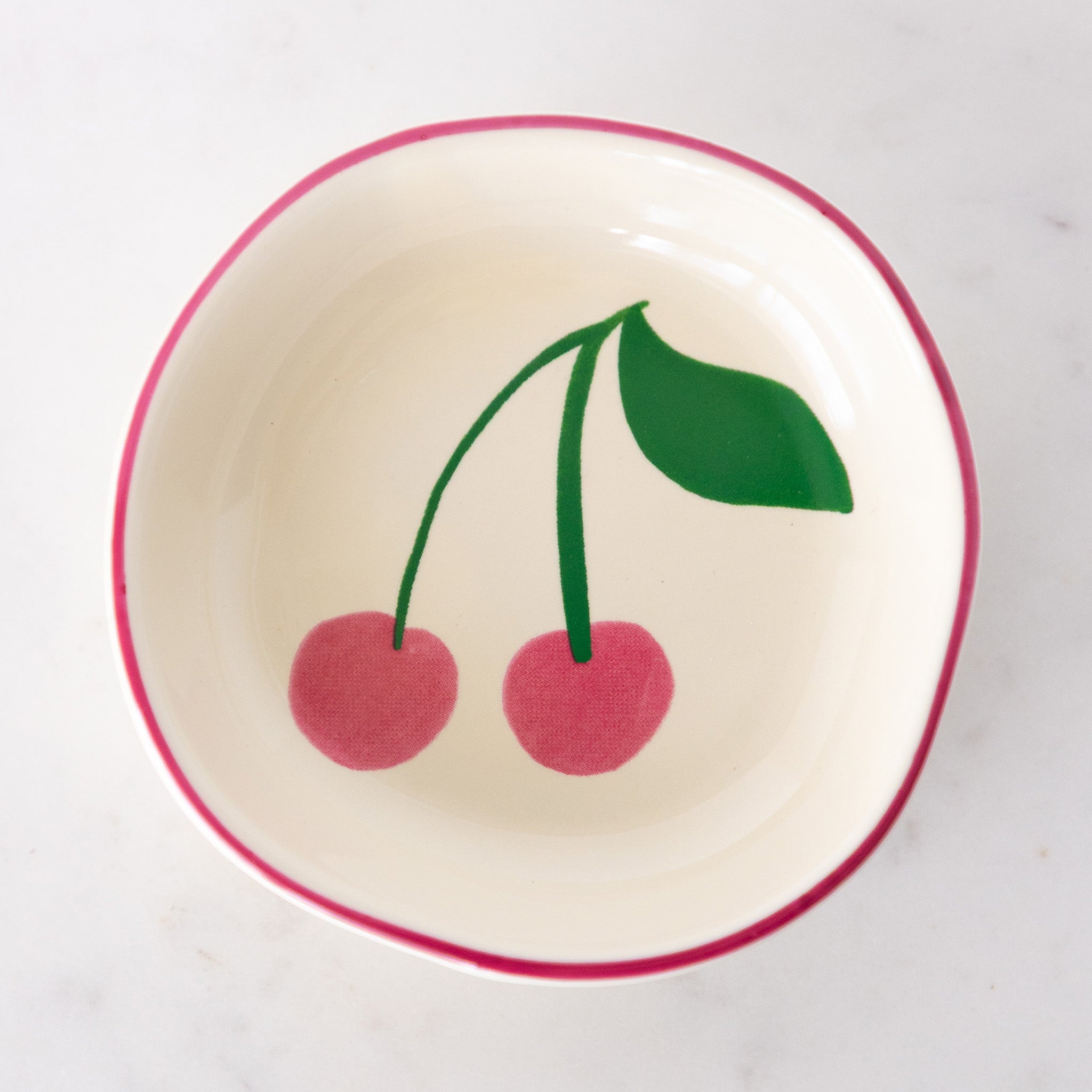A white ceramic pinch bowl with a pink rim features two painted pink cherries with a green leaf.