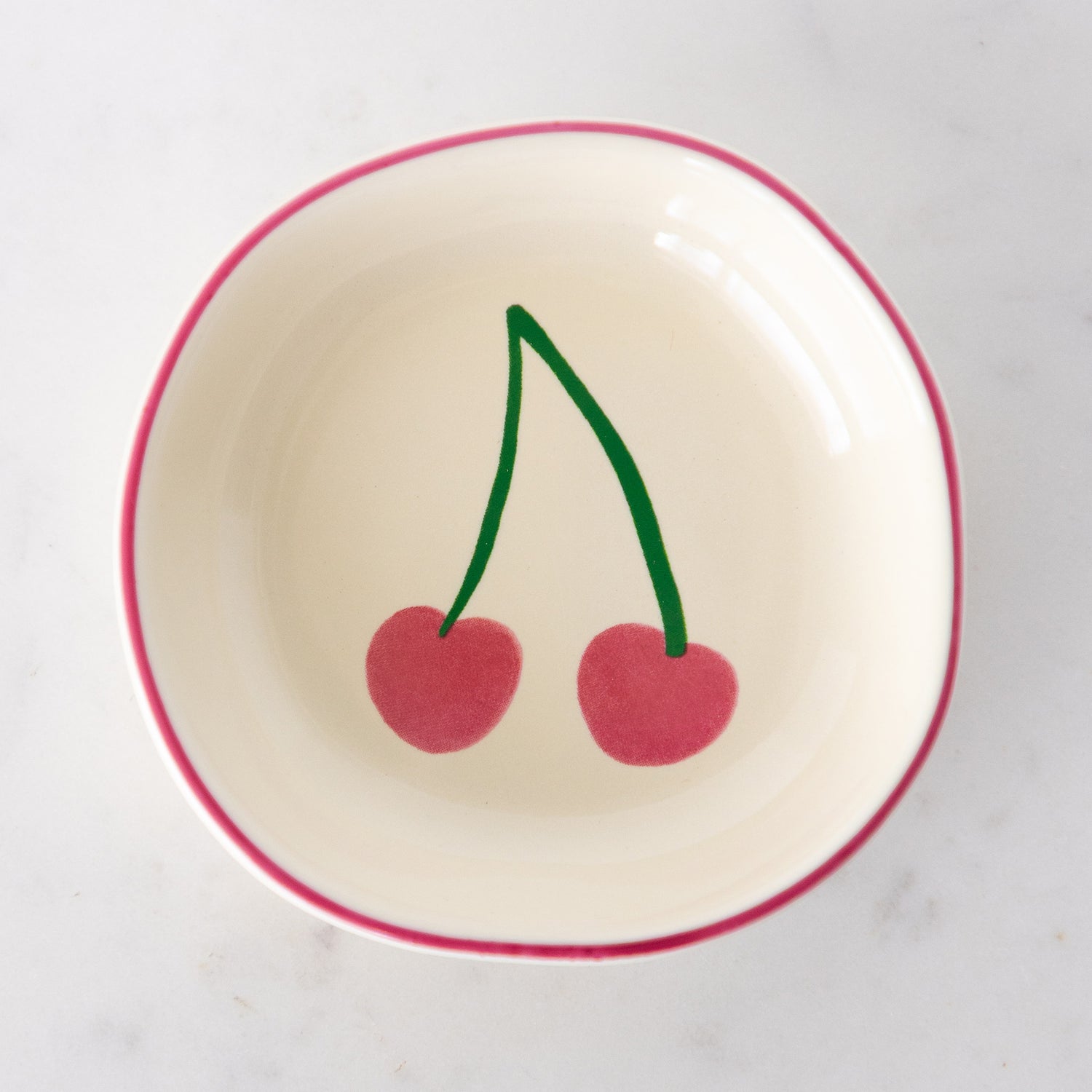 A white ceramic pinch bowl with a pink rim features two painted pink cherries.