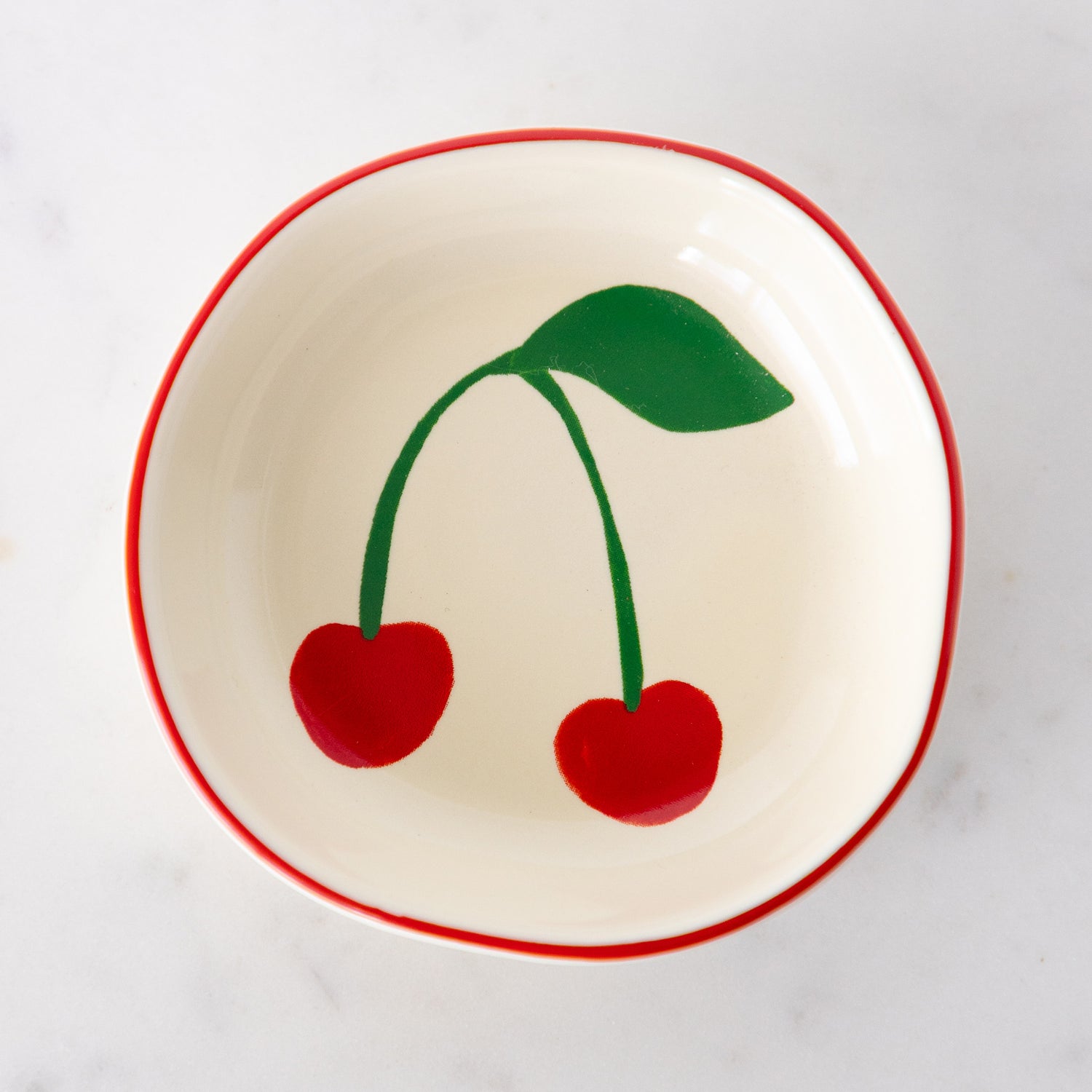 A white ceramic pinch bowl with a red rim features two painted bright red cherries with a green leaf.