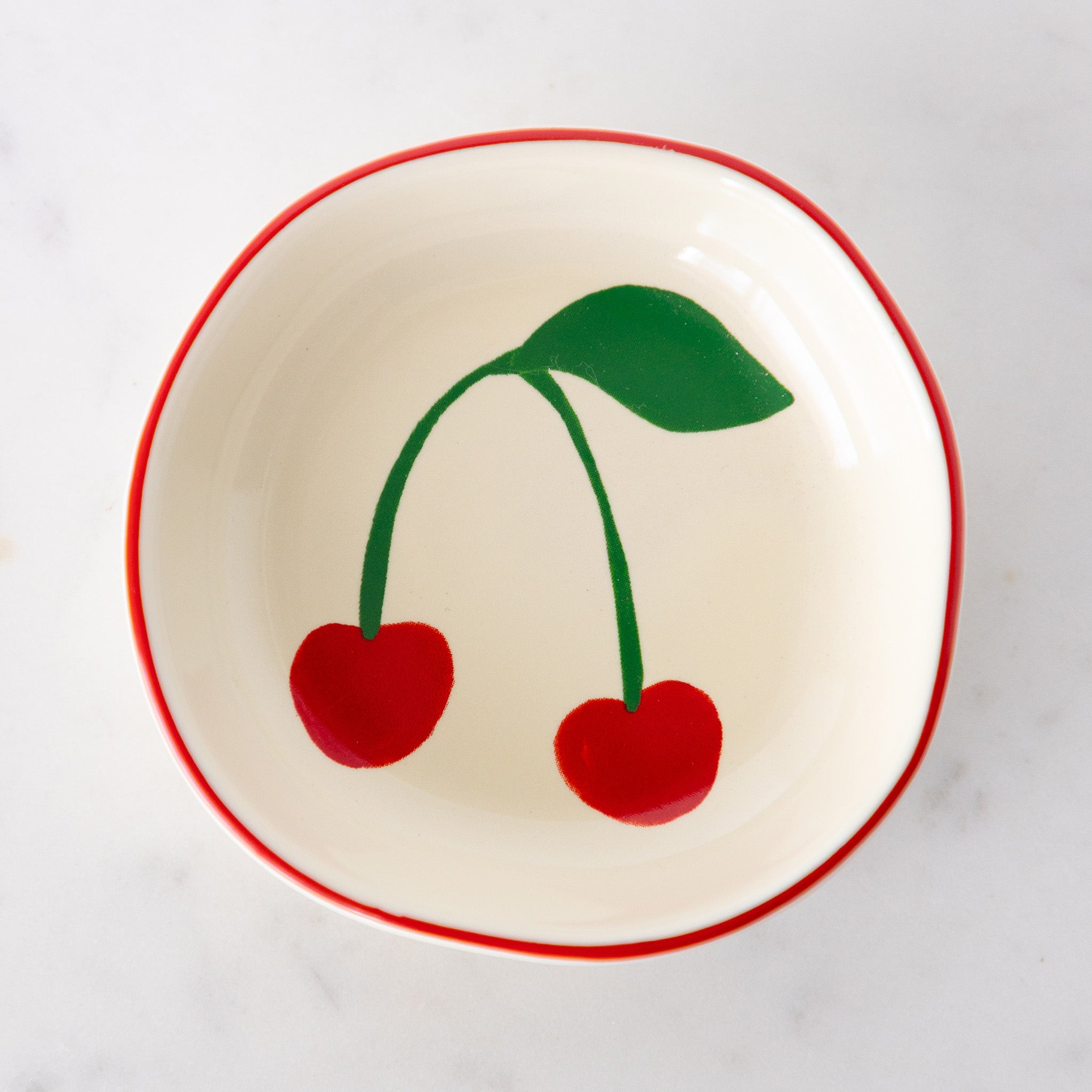 A white ceramic pinch bowl with a red rim features two painted bright red cherries with a green leaf.
