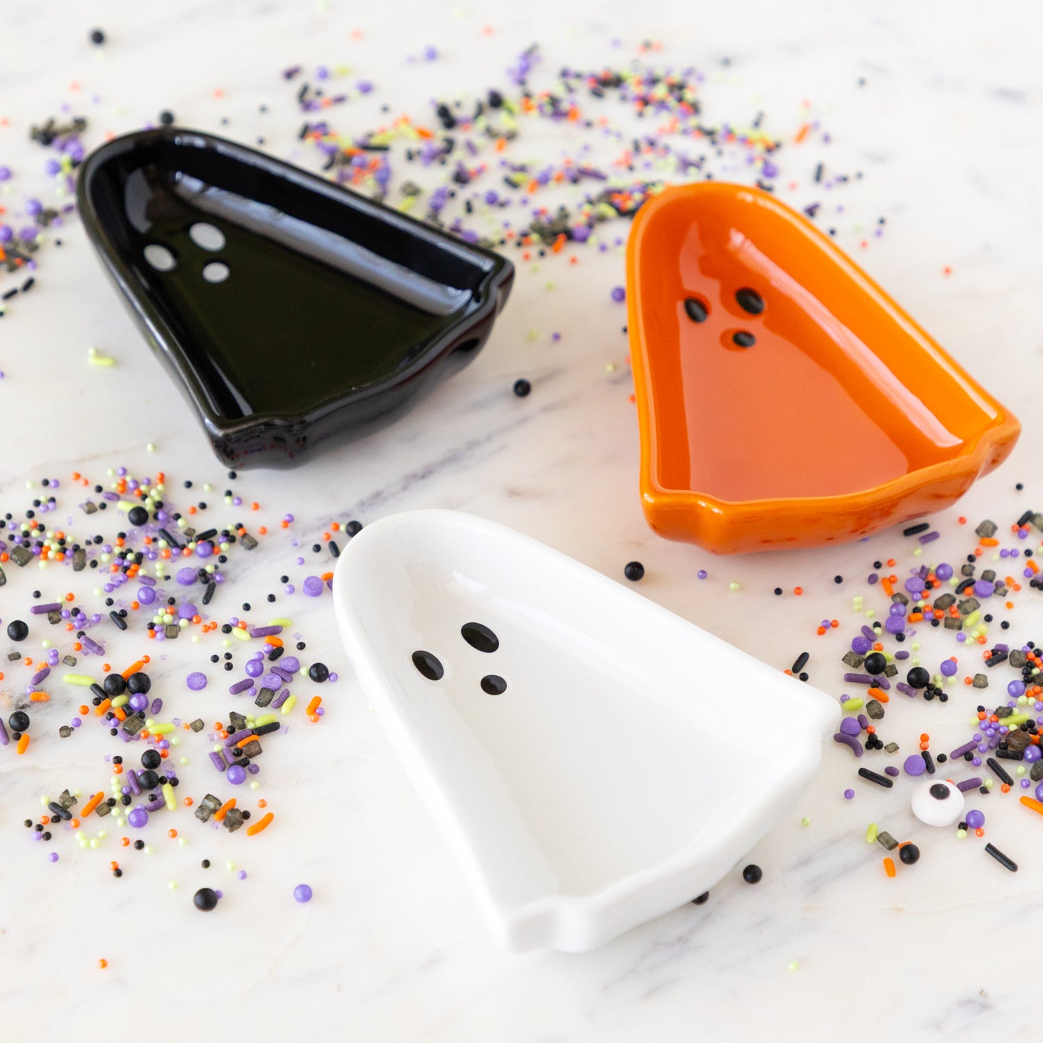 Kindred Spirits Ghost Pinch Bowls in orange, black and white on a marble table surrounded by Halloween sprinkles.