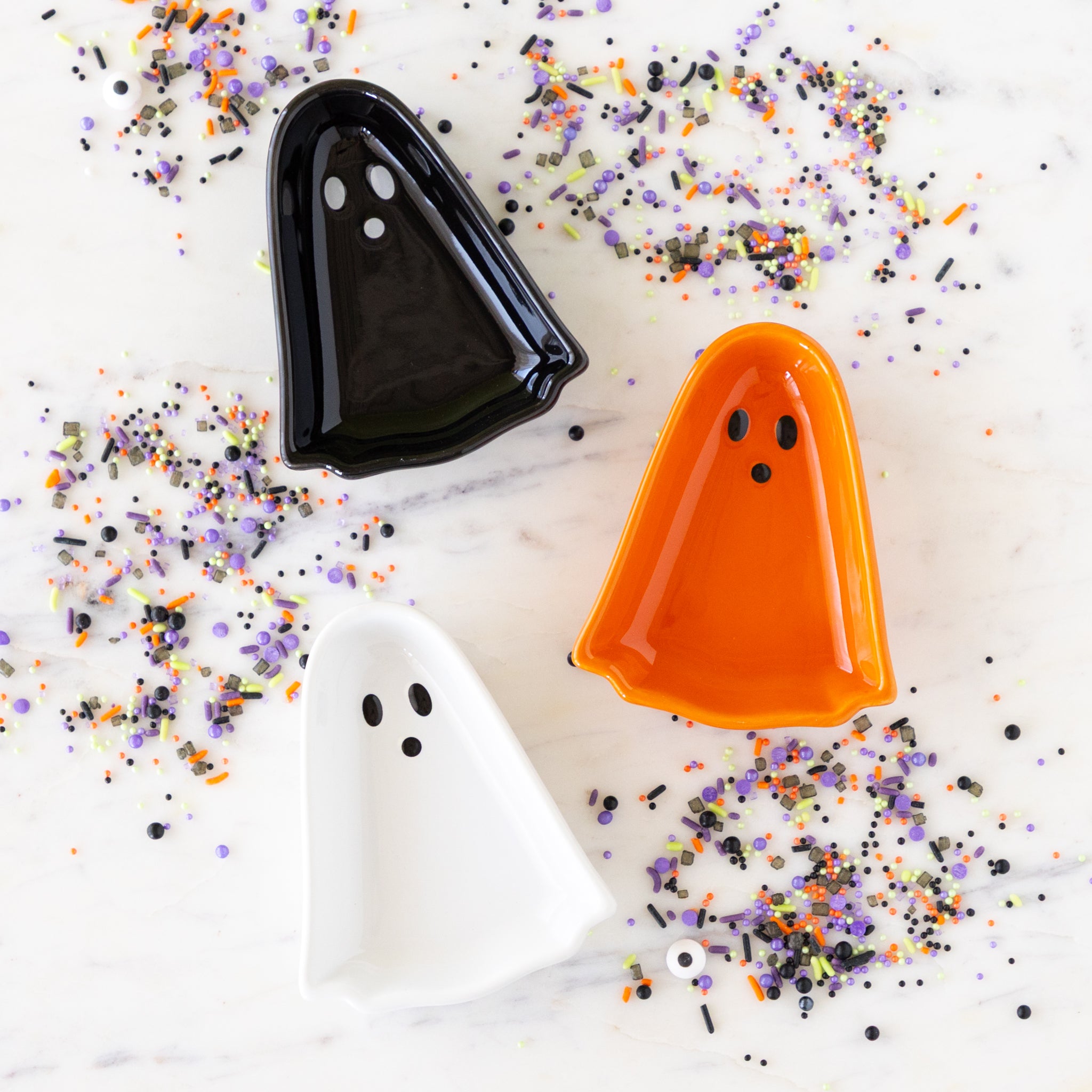 Kindred Spirits Ghost Pinch Bowls in orange, black and white on a marble table surrounded by Halloween sprinkles.