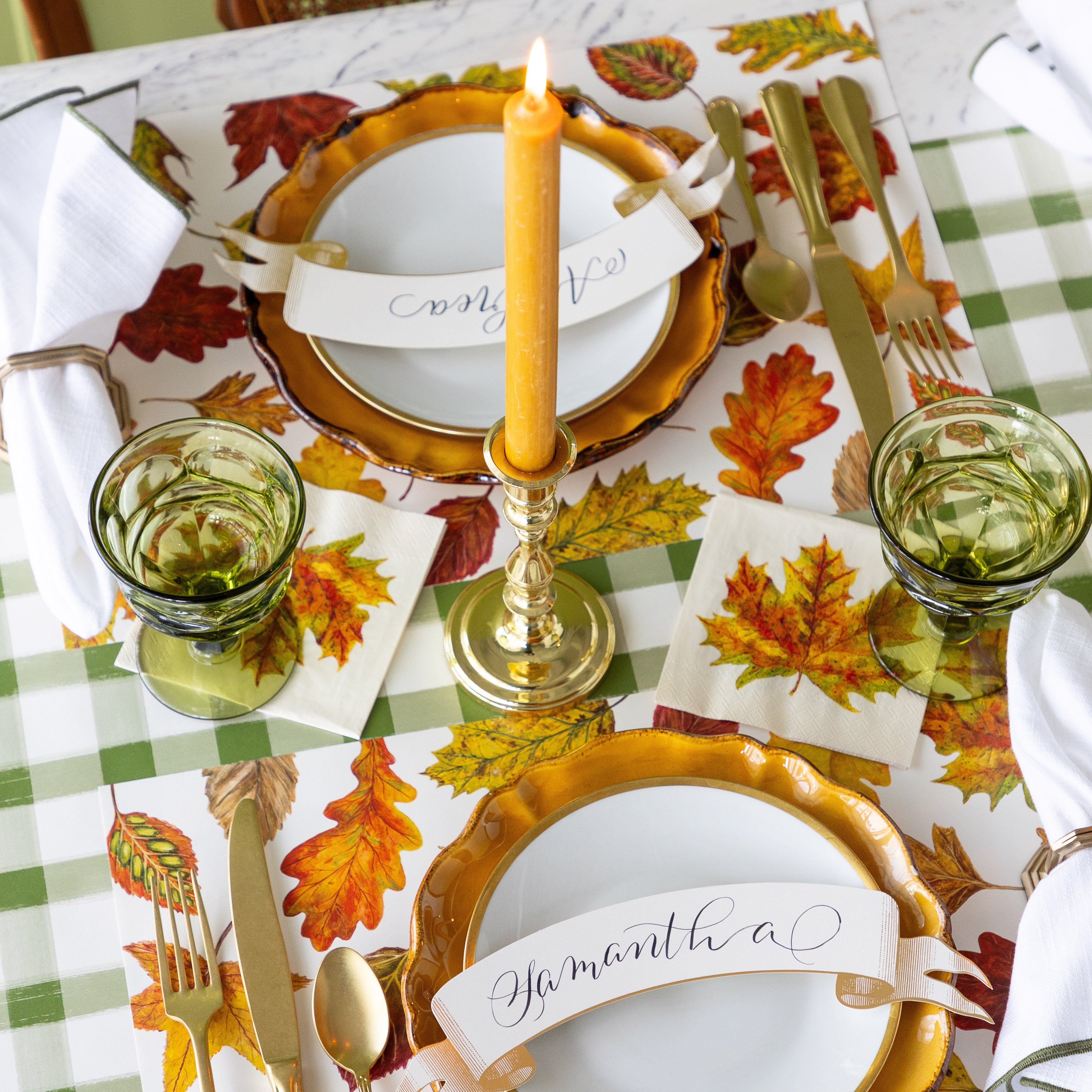 An elegant place setting with a lit candle in the middle featuring the Fall Foliage Cocktail Napkins under glasses, next to place settings with the Fall Foliage Placemats.
