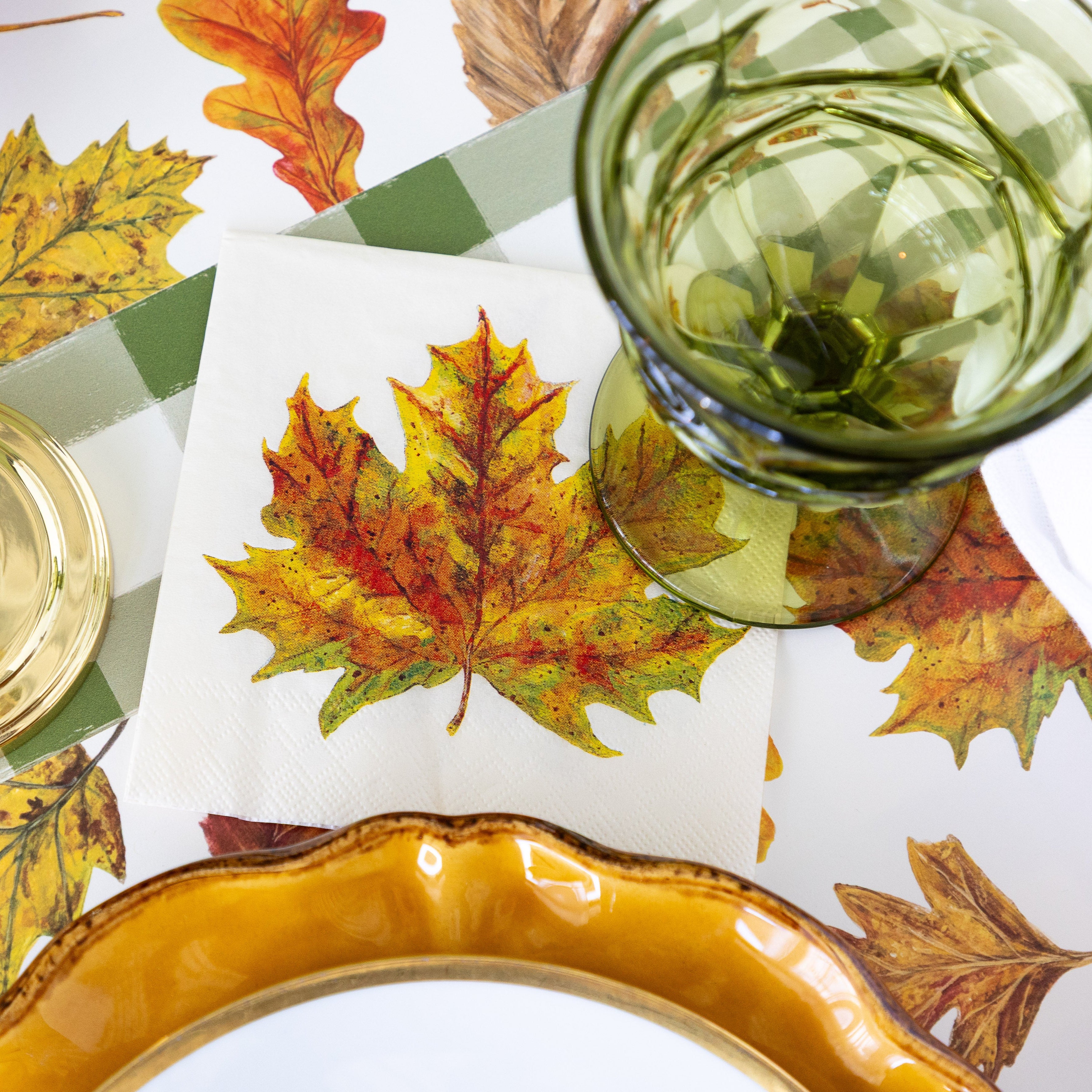 The Fall Foliage Cocktail napkin under a green glass, next to a place setting featuring the Fall Foliage Placemat and Green Painted Check Runner underneath.