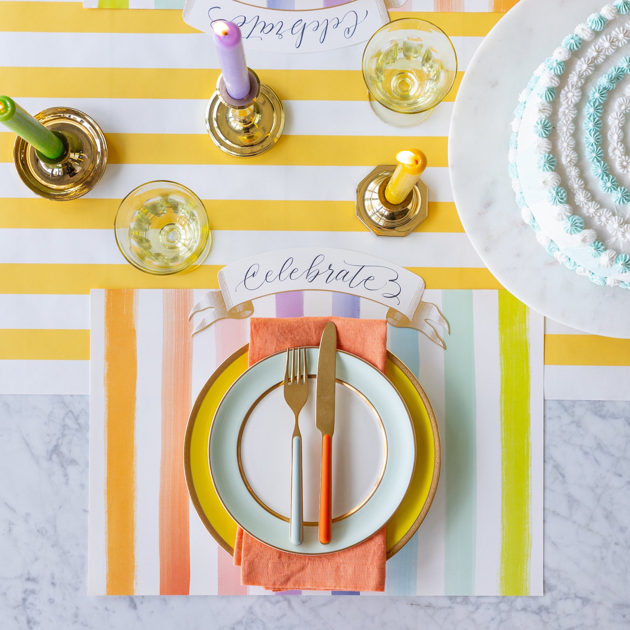 Colorful table setting with the Sorbet Painted Stripe Placemat, colorful plates and cutlery atop, and Classic Gold Banner Table Accent on the Marigold Classic Stripe Runner.