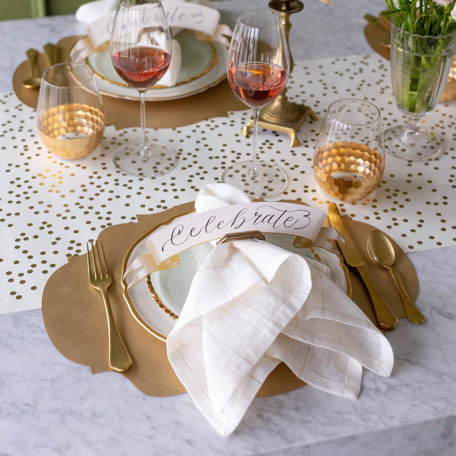 An elegant table setting featuring the Die-cut Gold French Frame Placemat, the Gold Banner Table Accent reading &quot;Celebrate&quot; in the Napkin Ring with Place Card Holder along with a napkin, and Gold Confetti Runner underneath.