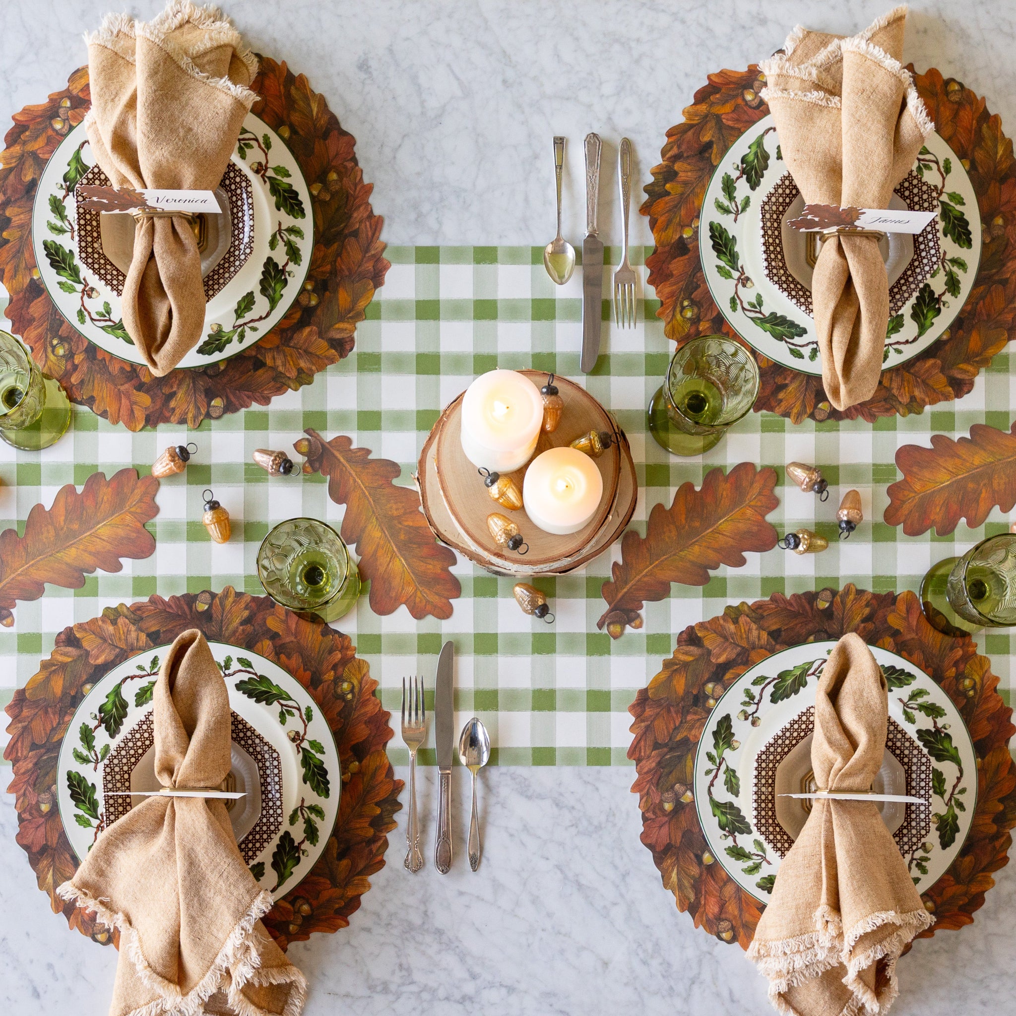 Thanksgiving table setting with Die-cut Autumn Wreath Placemats, Autumn Leaf Table Accents, candles, and Glass Acorn Ornaments on the Moss Painted Check Runner.