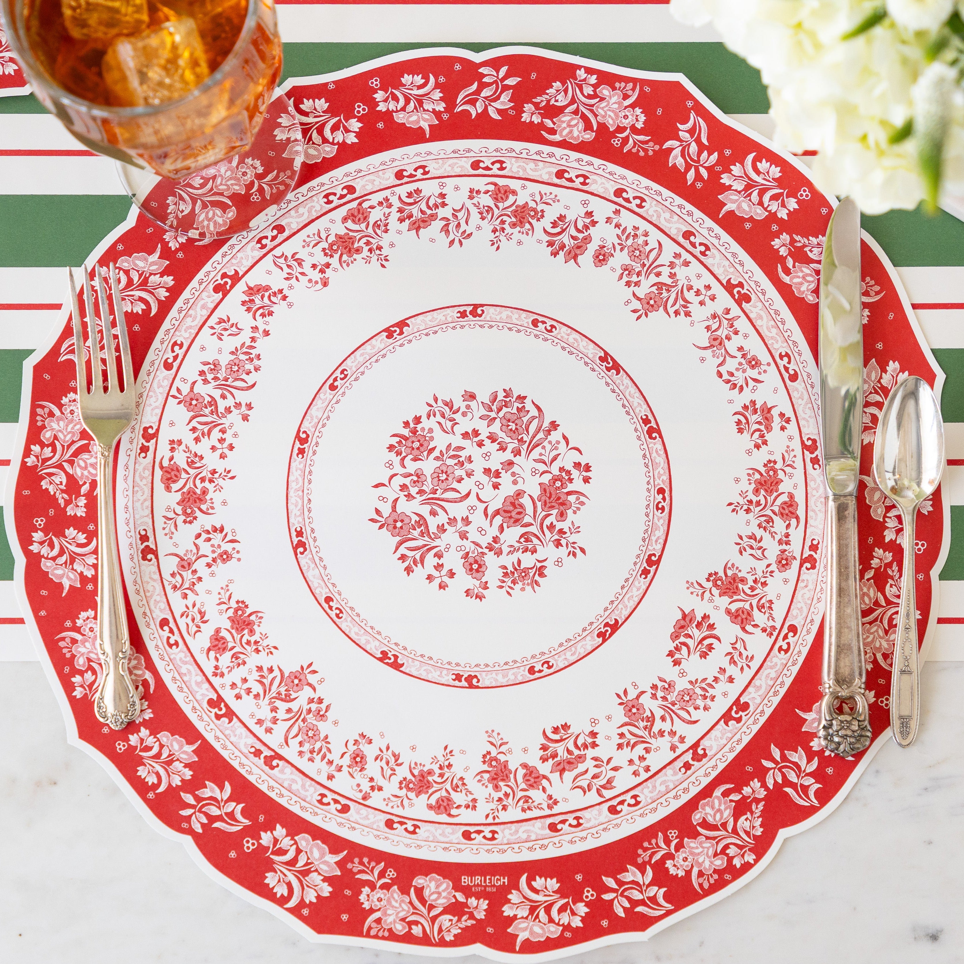 A place setting featuring the Die-cut Red Regal Placemat with vintage flatware and iced tea atop, and Green & Red Awning Stripe Runner underneath.