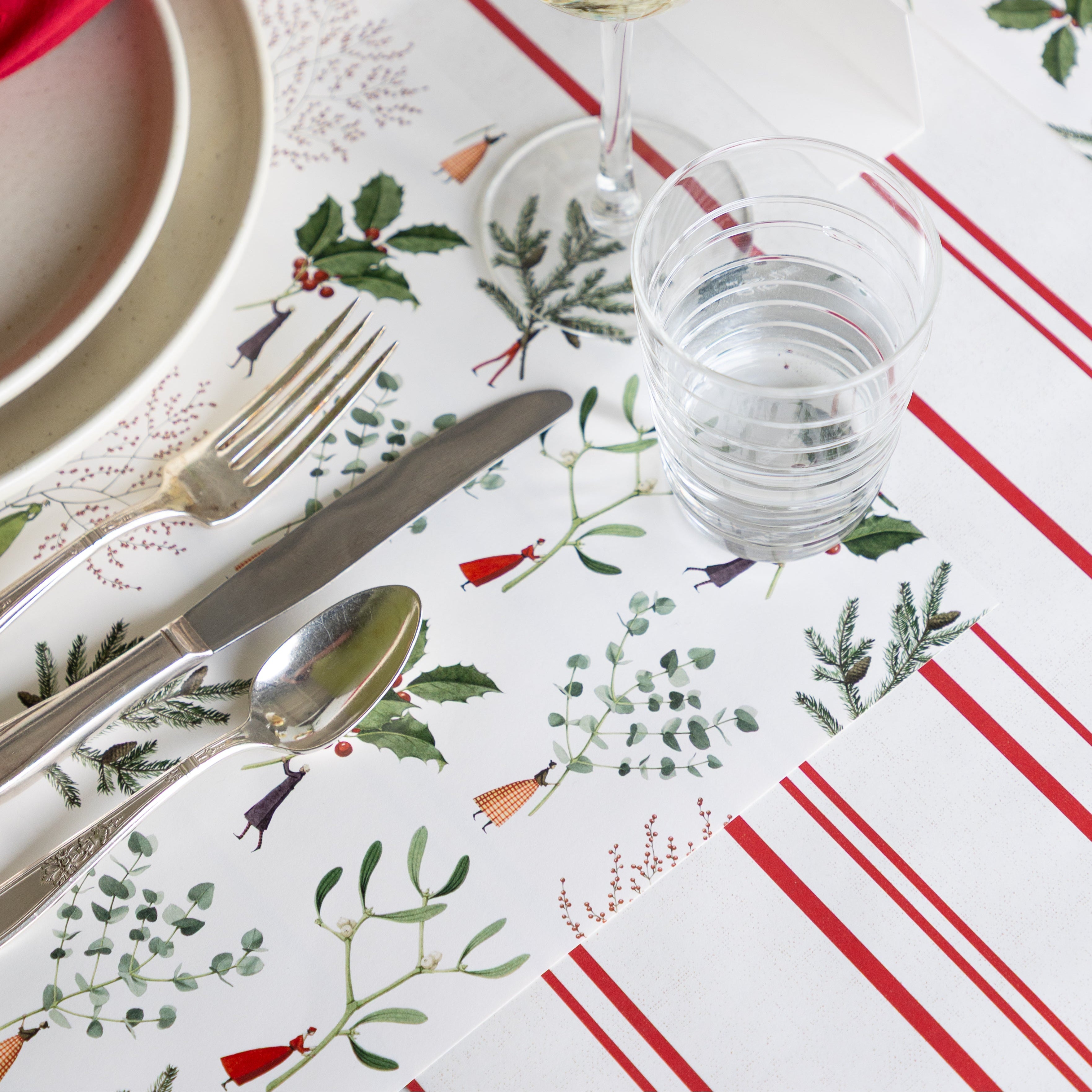 The Happy Christmas Placemat under vintage silverware, a glass of water and plates, and Antique Red Stripe Placemat underneath.