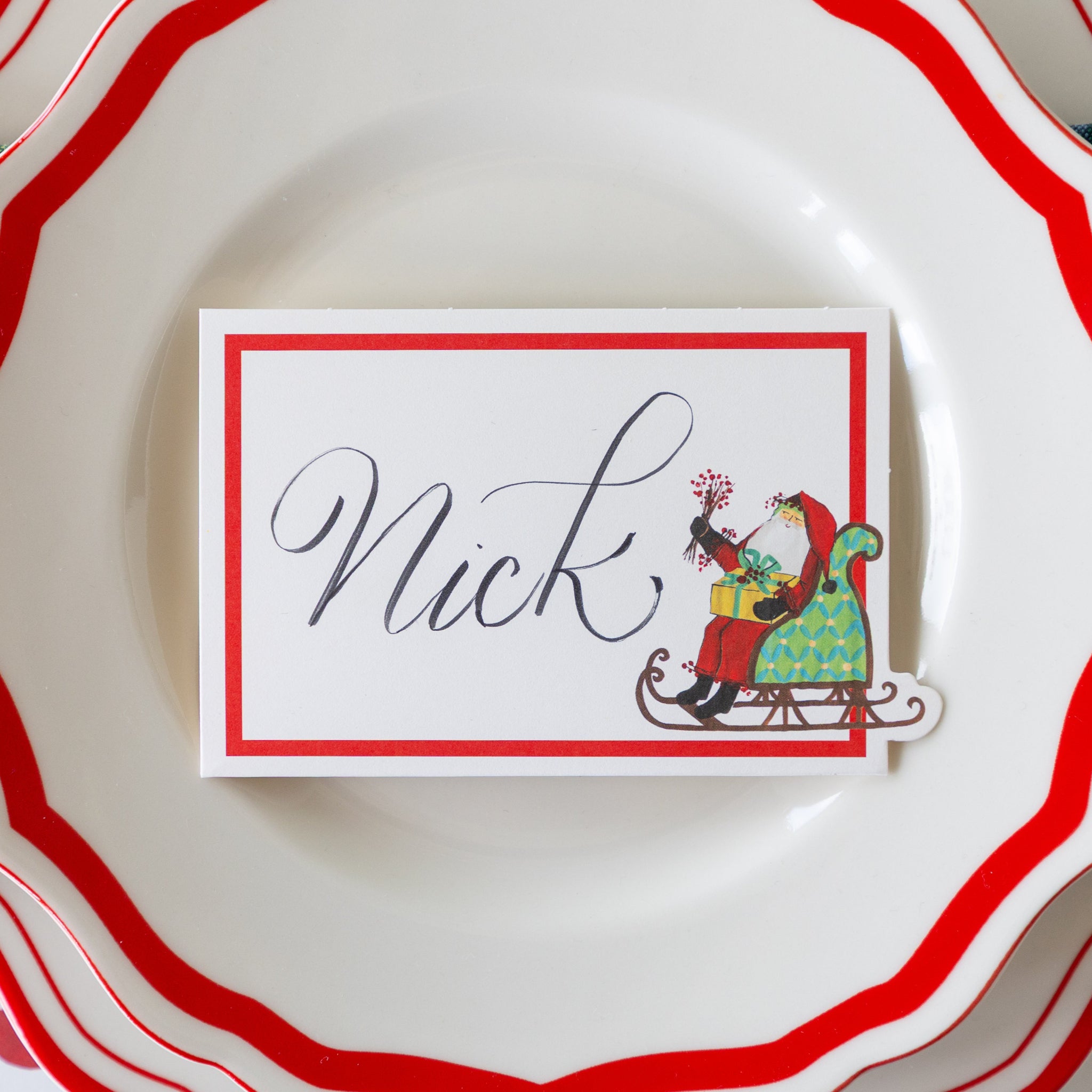 The Old St. Nick Sleigh Place Card with "Nick" written on it, atop the Red Icing on the Cake plates.