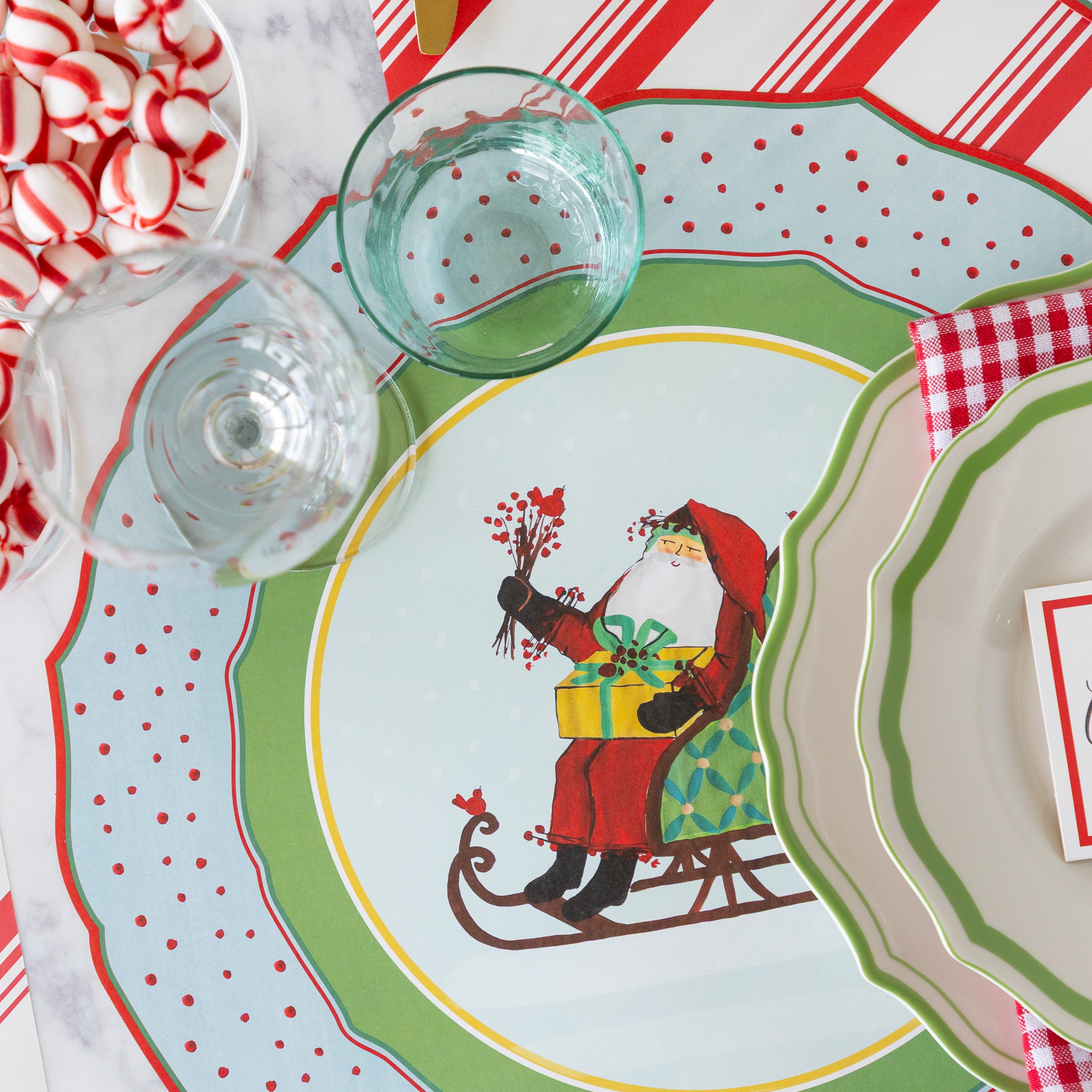 Christmas-themed table setting with Green Icing on the Cake plates, red-and-white checkered napkins and Die-cut Old St. Nick Sleigh Placemat on the Peppermint Stripe Runner.