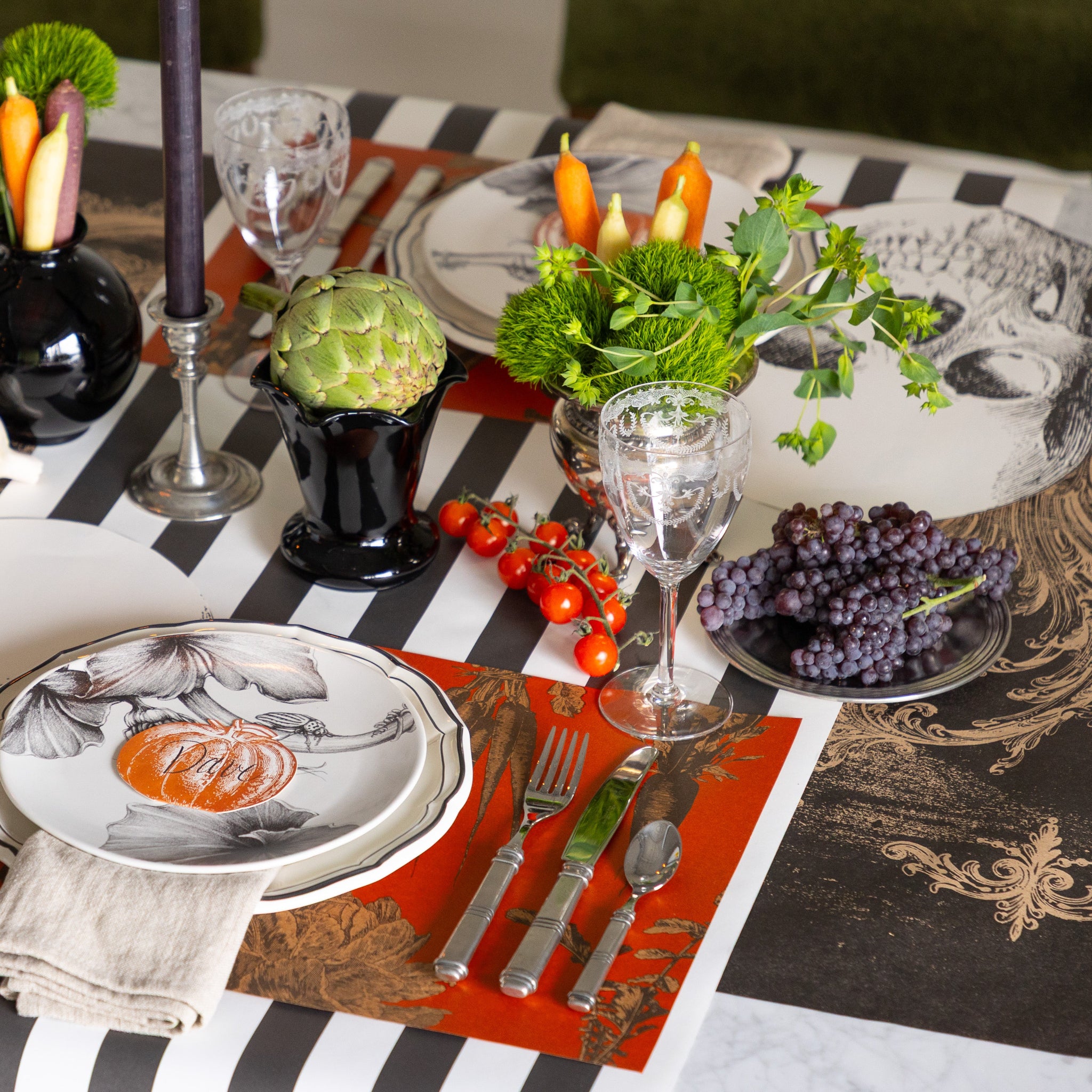 A Halloween themed table setting with the Black Archival Runner under the Black Classic Stripe Runner, fruits & veggies, Harvest Vegetable Persimmon Placemat and Skull Placemat.