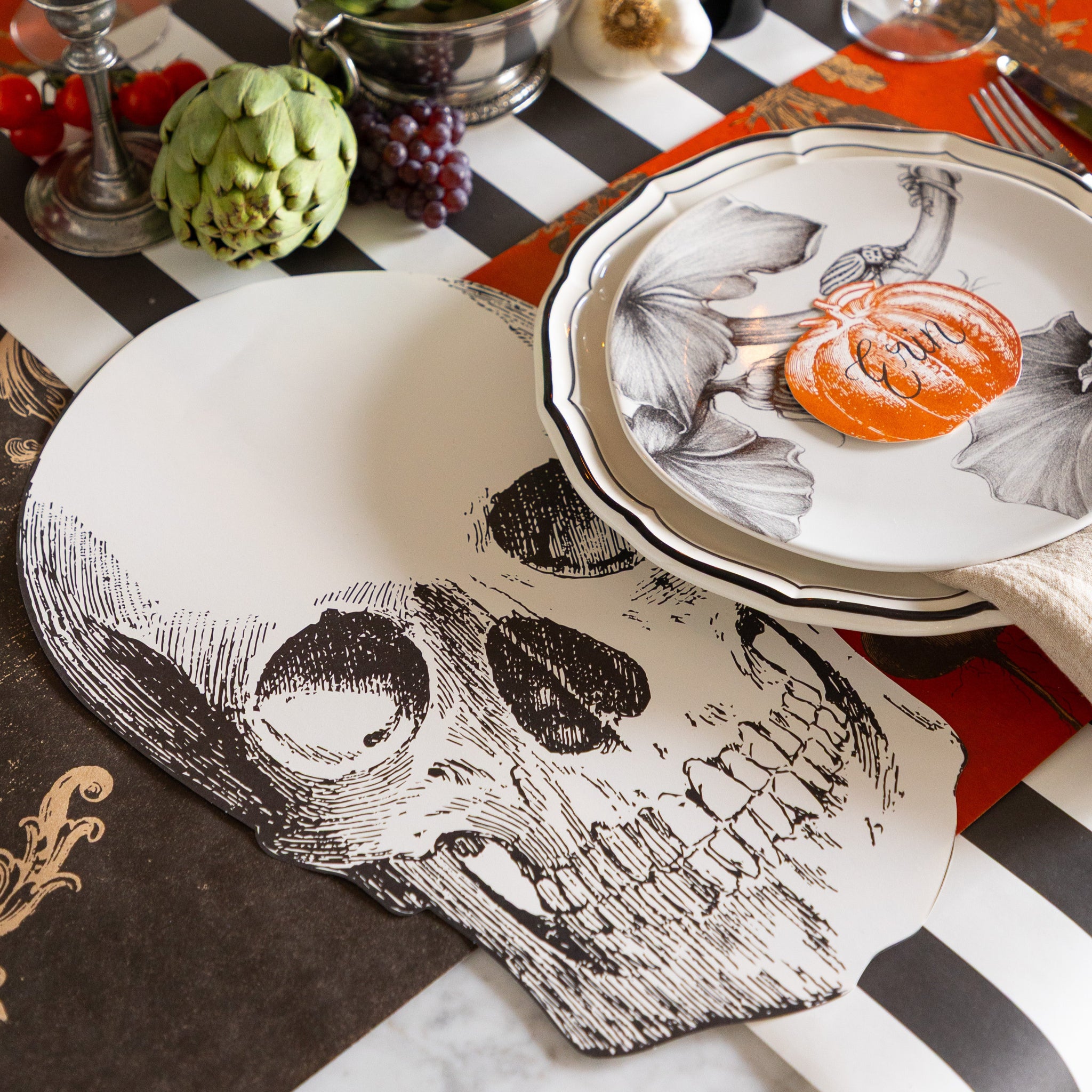 Halloween-themed table setting with the Die-cut Skull Placemat, Pumpkin Place Card and Harvest Vegetable Persimmon Placemat on the Black Classic Stripe and Archival Black Runner.