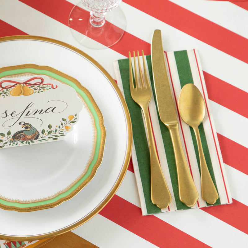 A Green & Red Awning Stripe Guest napkin under gold cutlery in a festive holiday place setting.