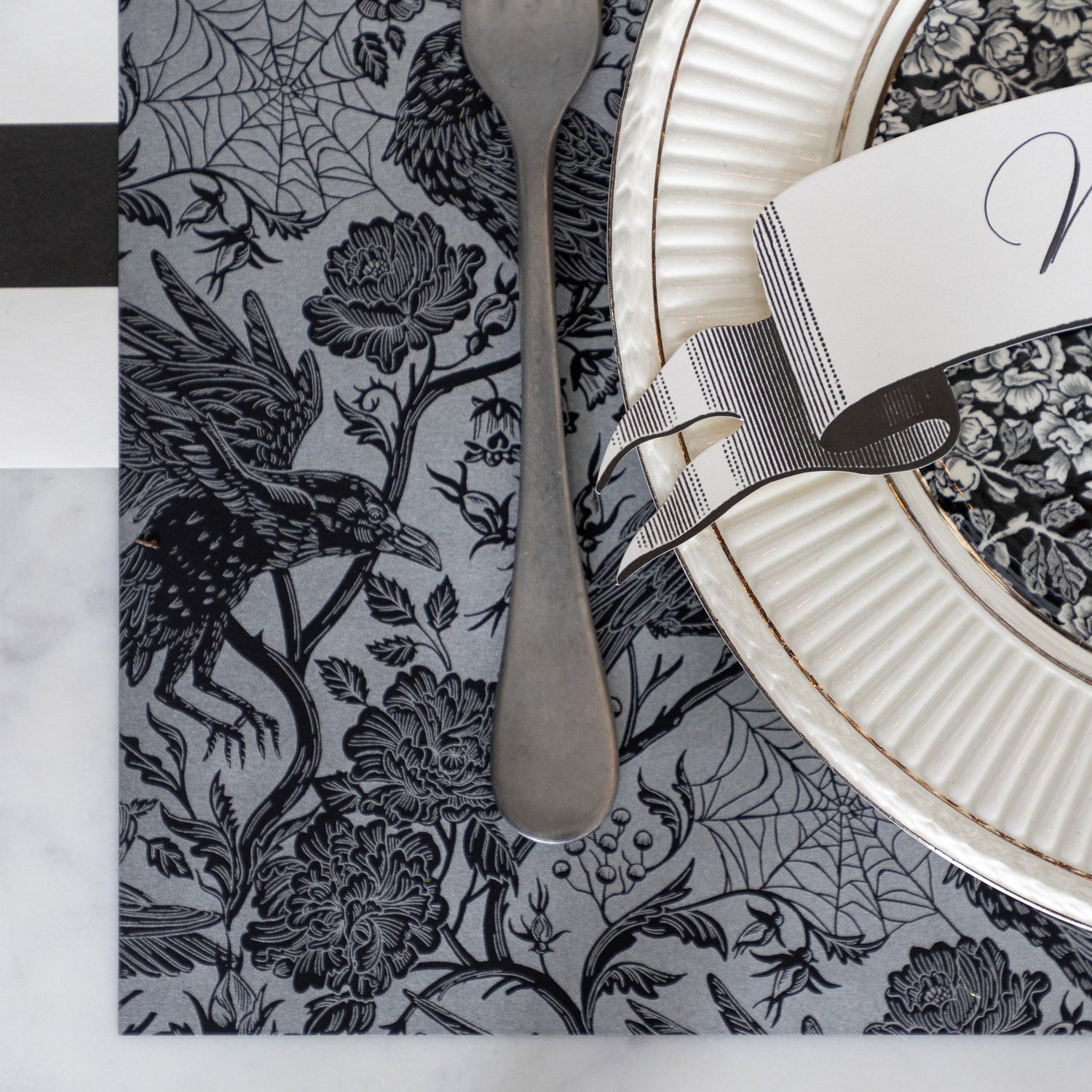 A place setting featuring the Raven Toile Placemat with a silver fork and plates on top and Black Classic Stripe Runner underneath.