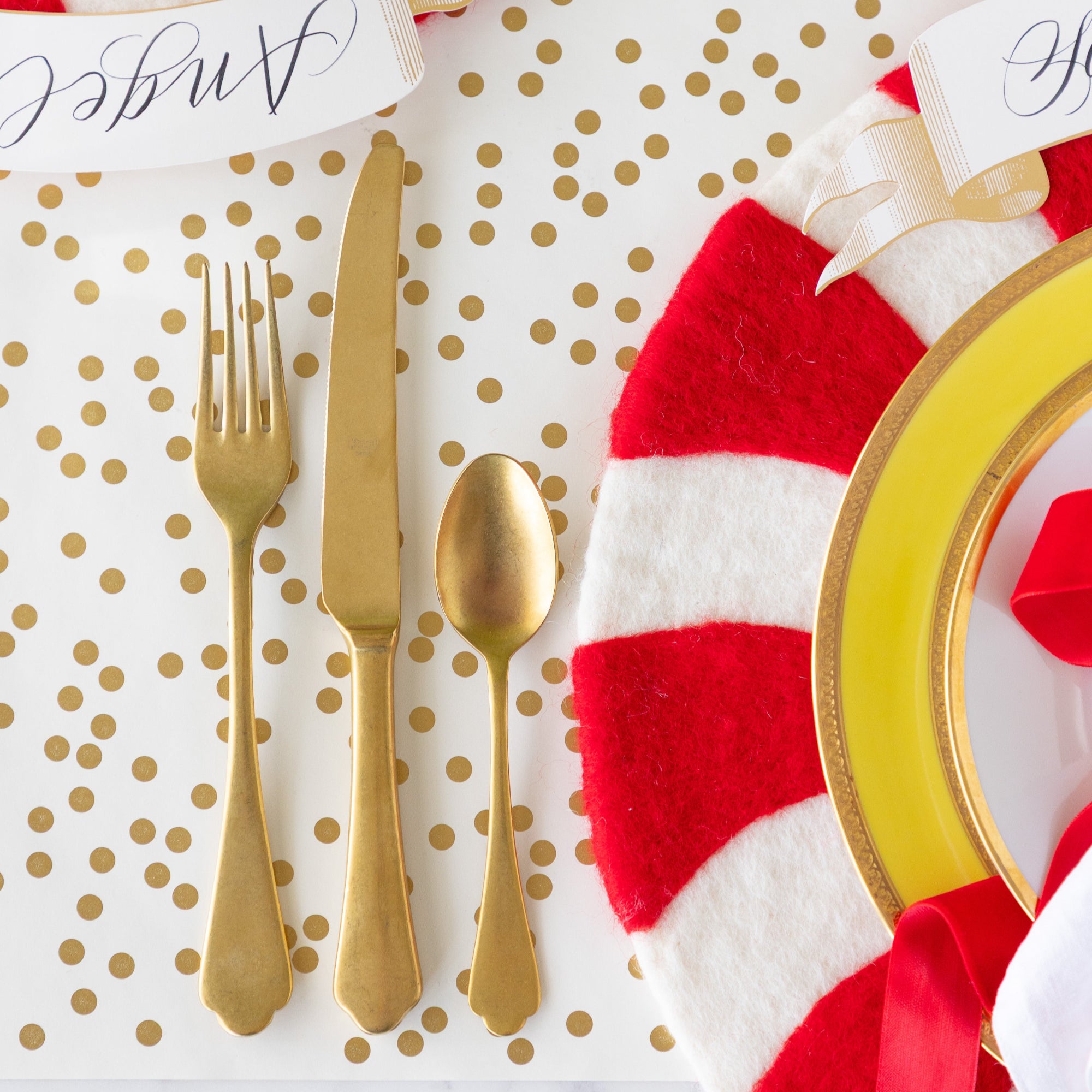 A place setting with a gold fork, knife and spoon next to the Red Felt Candy Stripe Placemat, on the Gold Confetti Runner.