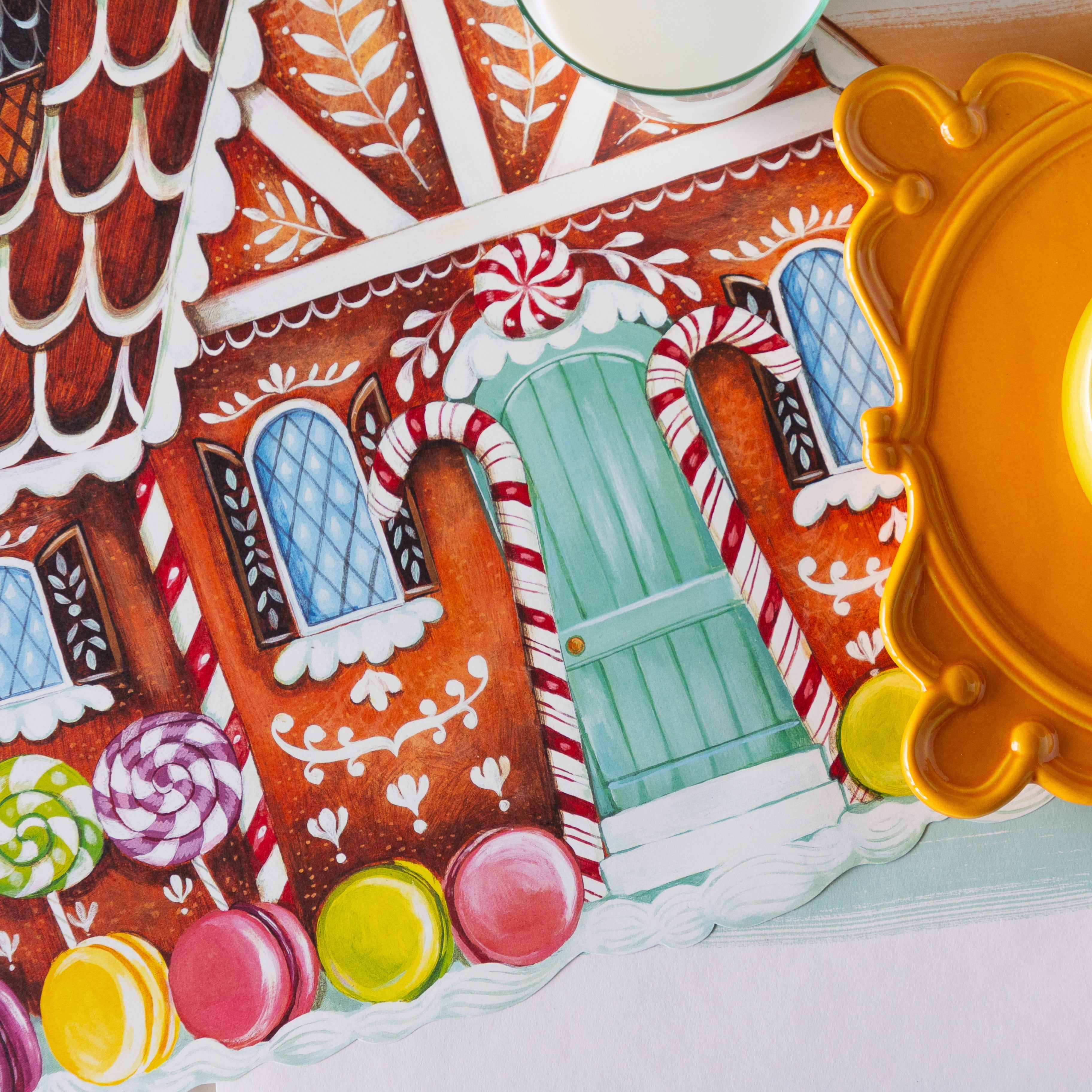 A close up of the Die-cut Gingerbread House Placemat showing the hand-painted details of macaroons, lollipops and candy canes framing the door.