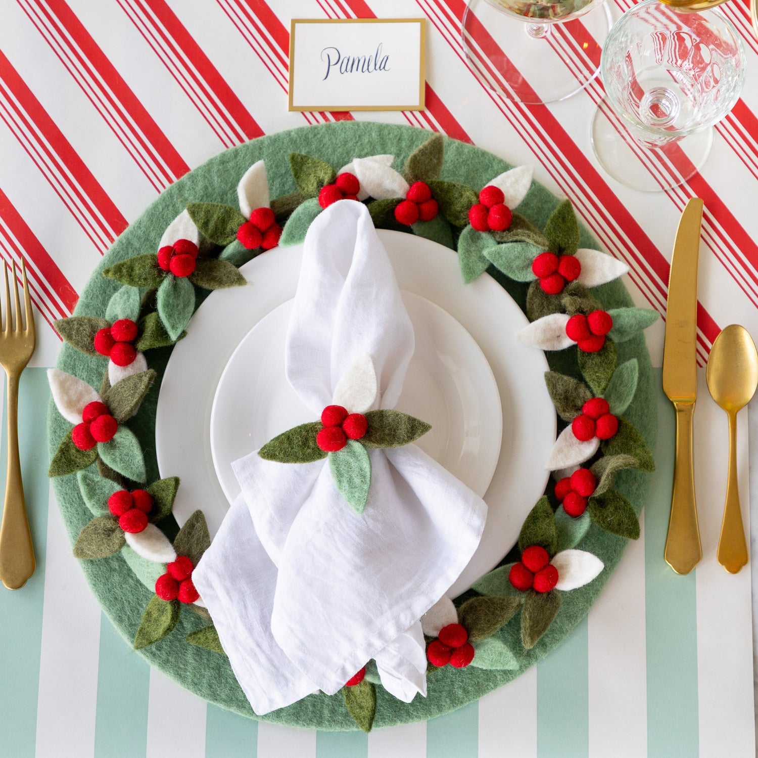 A place setting featuring the Mint Felt Placemat with white plates, a napkin tied in the Felt Berry Napkin Ring and Felt Berry Wreath Charger atop, and Gold Frame Place Card above, on the Candy Stripe Runner and Seafoam Classic Stripe Runner.