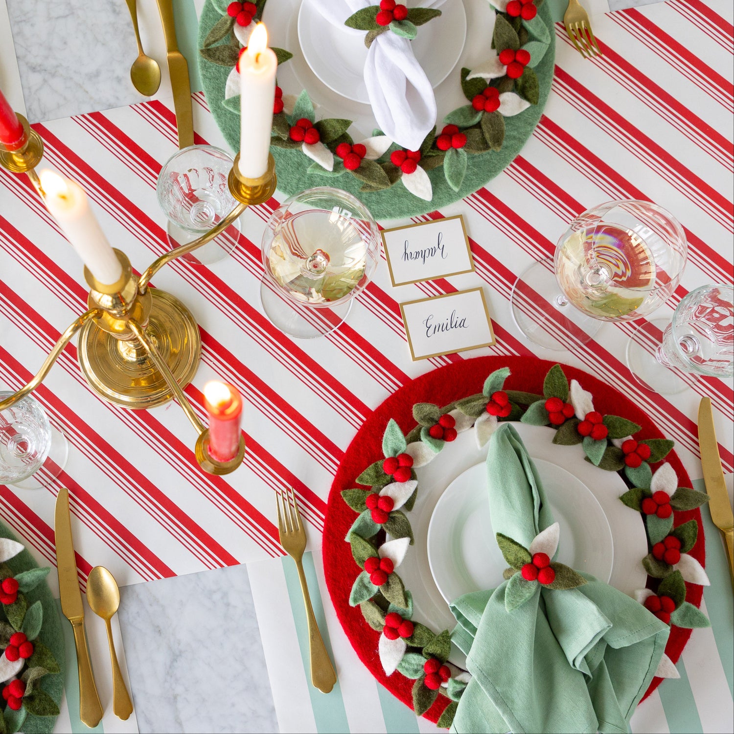 A festive dining table set with Mint Felt Placemats, Felt Berry Chargers, Felt Berry Napkin Rings, gold cutlery, Gold Frame Place Cards, wine glasses, and red and white candles in a gold candelabra on the Peppermint Stripe and Seafoam Classic Stripe Runner.