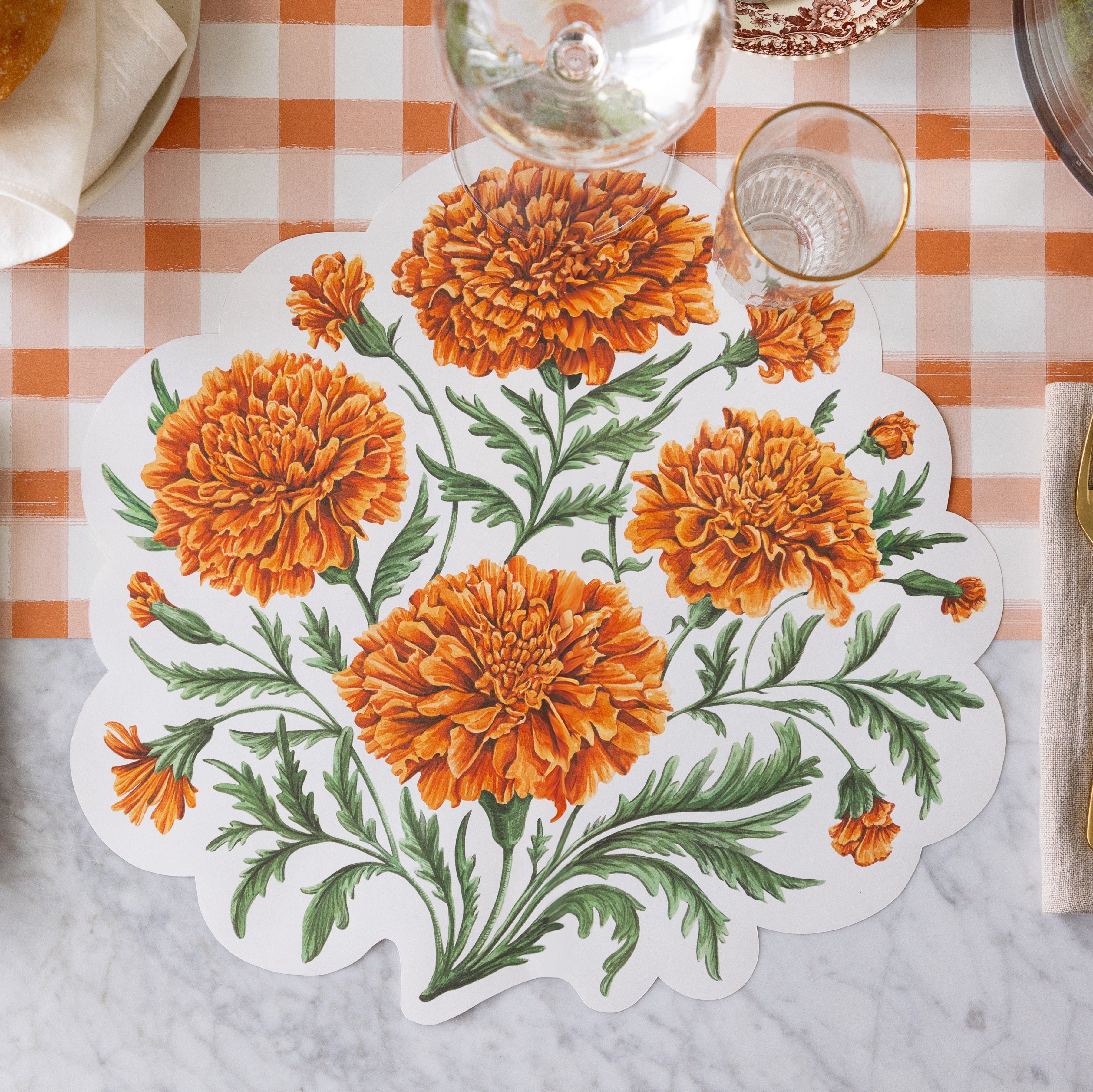 The Die-cut Marigold Bouquet Placemat with a wine and water glass slightly overtop it and Orange Painted Check Runner underneath.