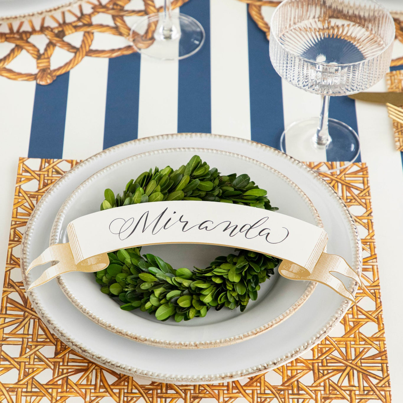 Classic Gold Banner Table Accent with "Miranda" written on it, on stack of plates on a rattan themed place setting.