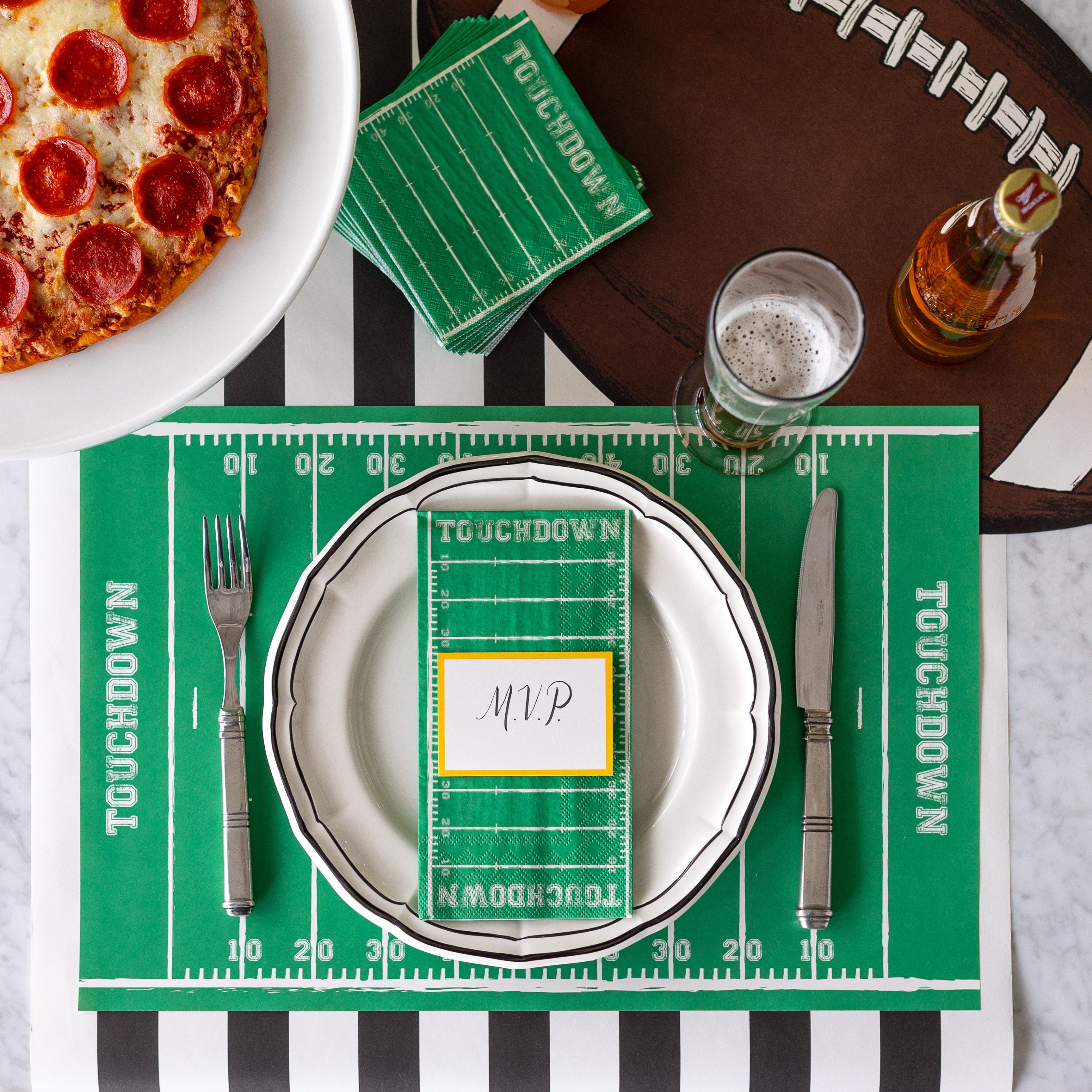 A football themed place setting with the Touchdown Guest Napkin resting on the dinner plate with a place card on top.