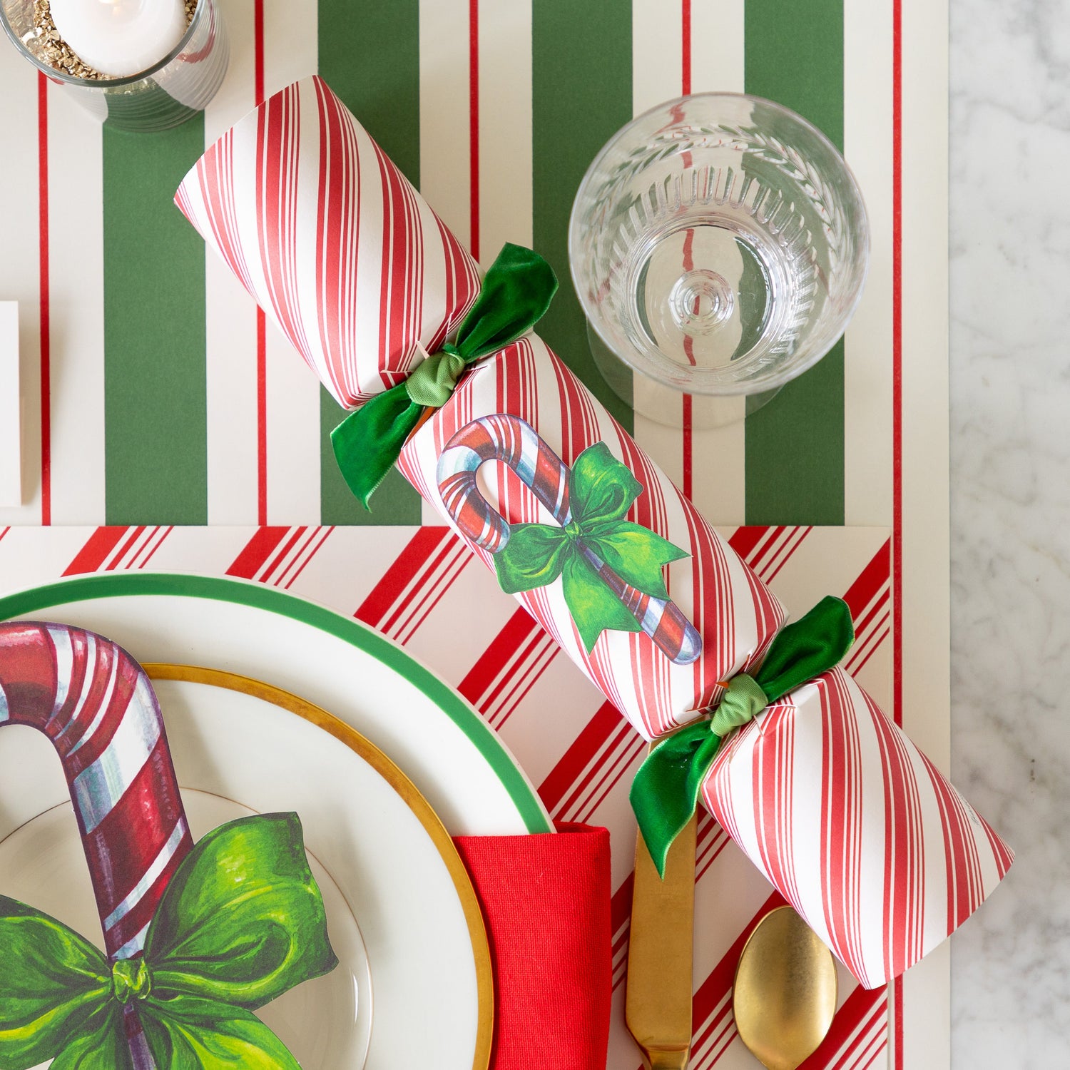 The Candy Cane Cracker next a place setting featuring the Peppermint Stripe Placemat, and Green &amp; Red Awning Stripe Runner underneath.