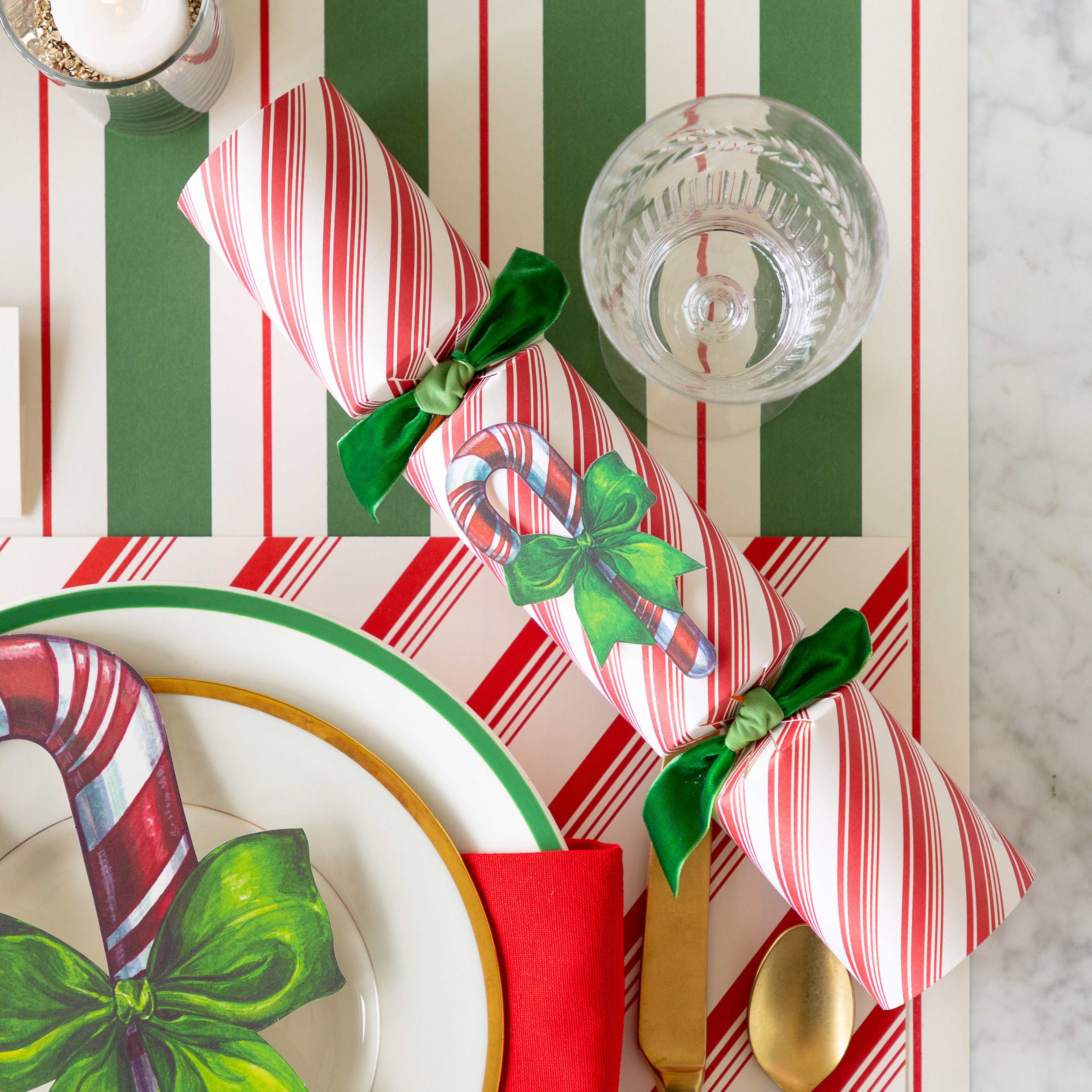 The Candy Cane Cracker next a place setting featuring the Peppermint Stripe Placemat, and Green &amp; Red Awning Stripe Runner underneath.