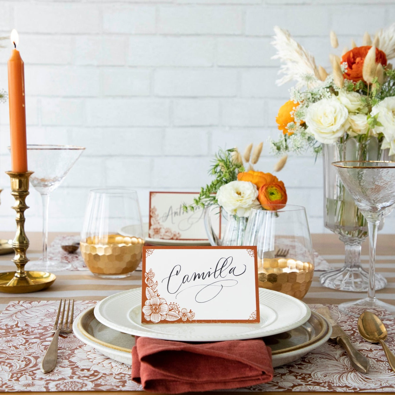 A free-standing, rectangular white table card with a dark orange frame around the edges, embellished with dark orange linework flower designs in the corners.