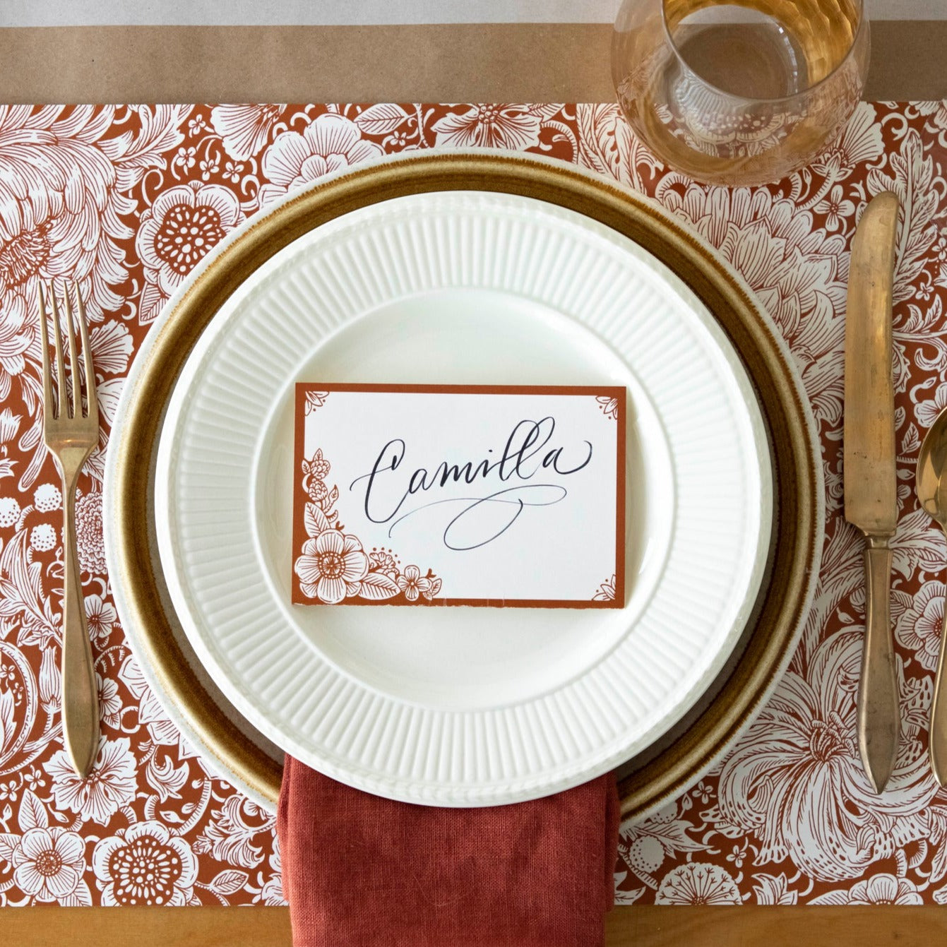 A free-standing, rectangular white table card with a dark orange frame around the edges, embellished with dark orange linework flower designs in the corners.