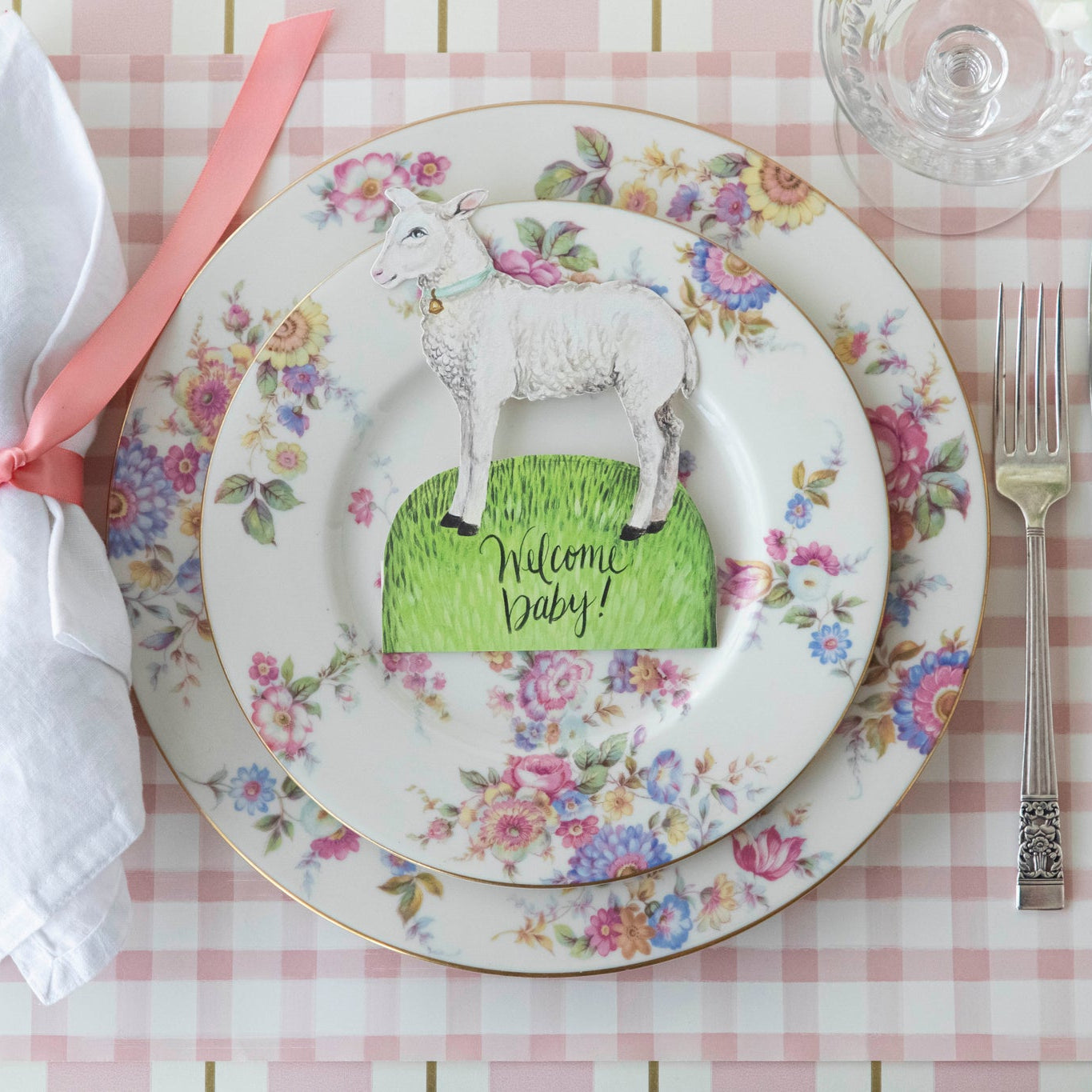 Welcome Little Lamb Place Card with "Welcome Baby" written on it, centered on dinner plates on a place setting for one.