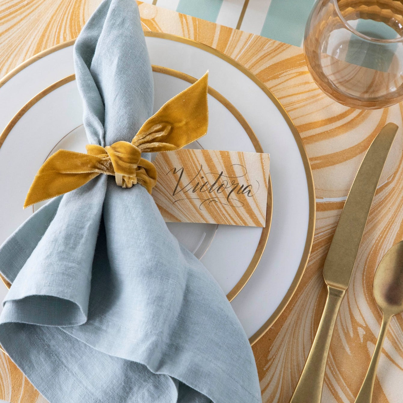 A Gold and cream gift tag tied to the napkin at a place setting, labeled "Victoria".