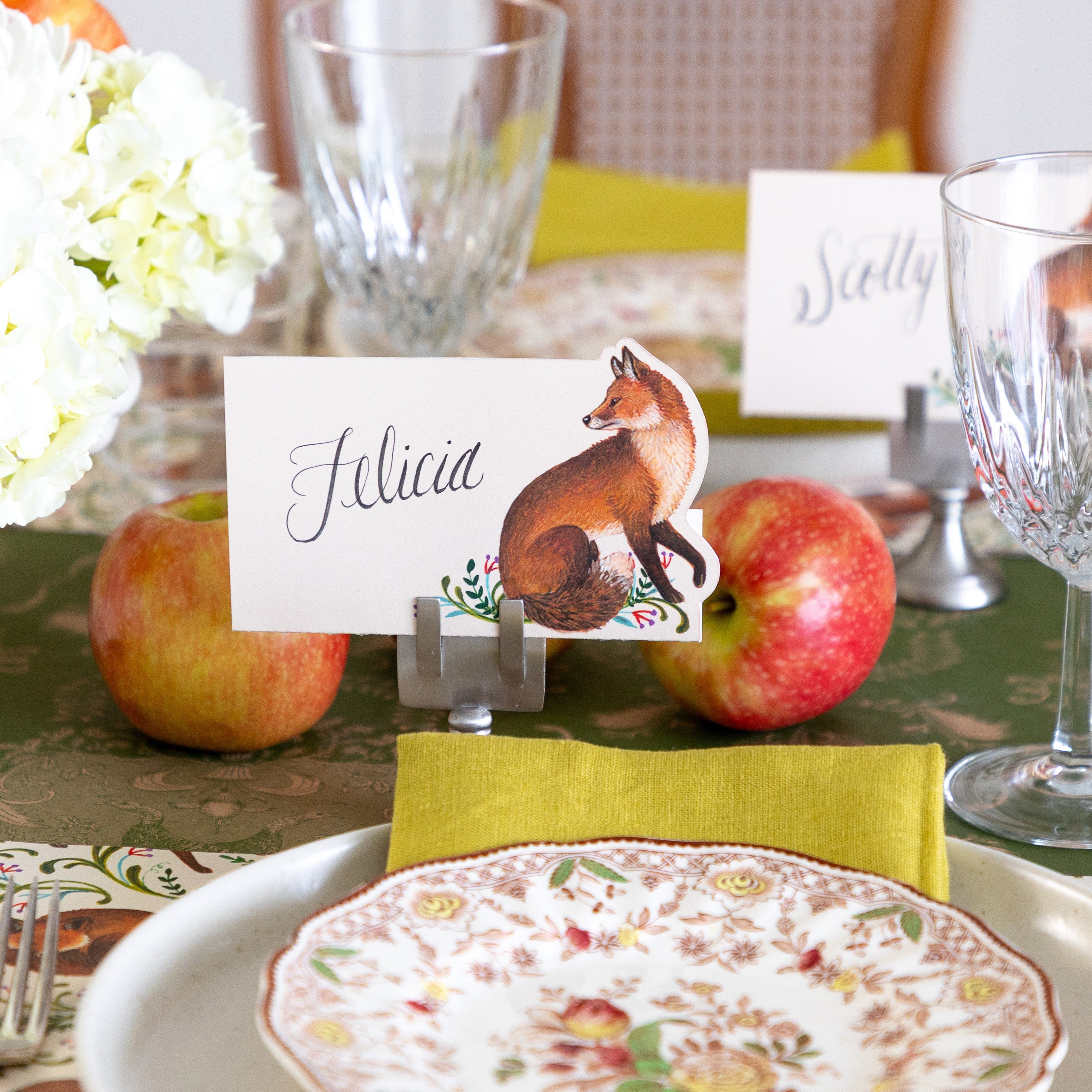 The Fanciful Fox Place Card reading "Felicia" held by the Silver Place Card Holder, behind an elegant place setting.