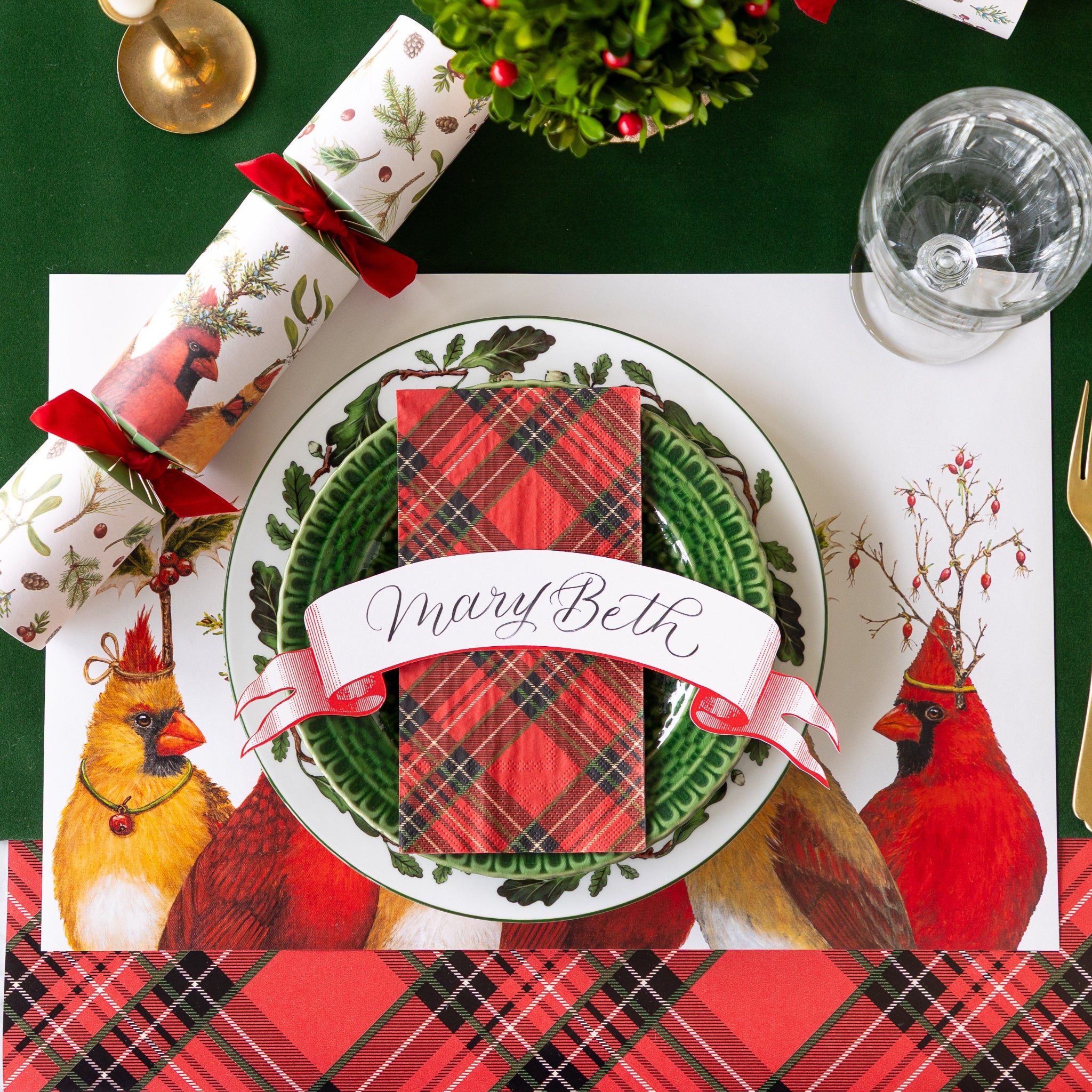 A festive place setting featuring the Cardinal Party Placemat with vintage dinnerware, Red Plaid Guest Napkin and Red Classic Banner Table Accent atop, on the Red Plaid and Green Flocked Runner.