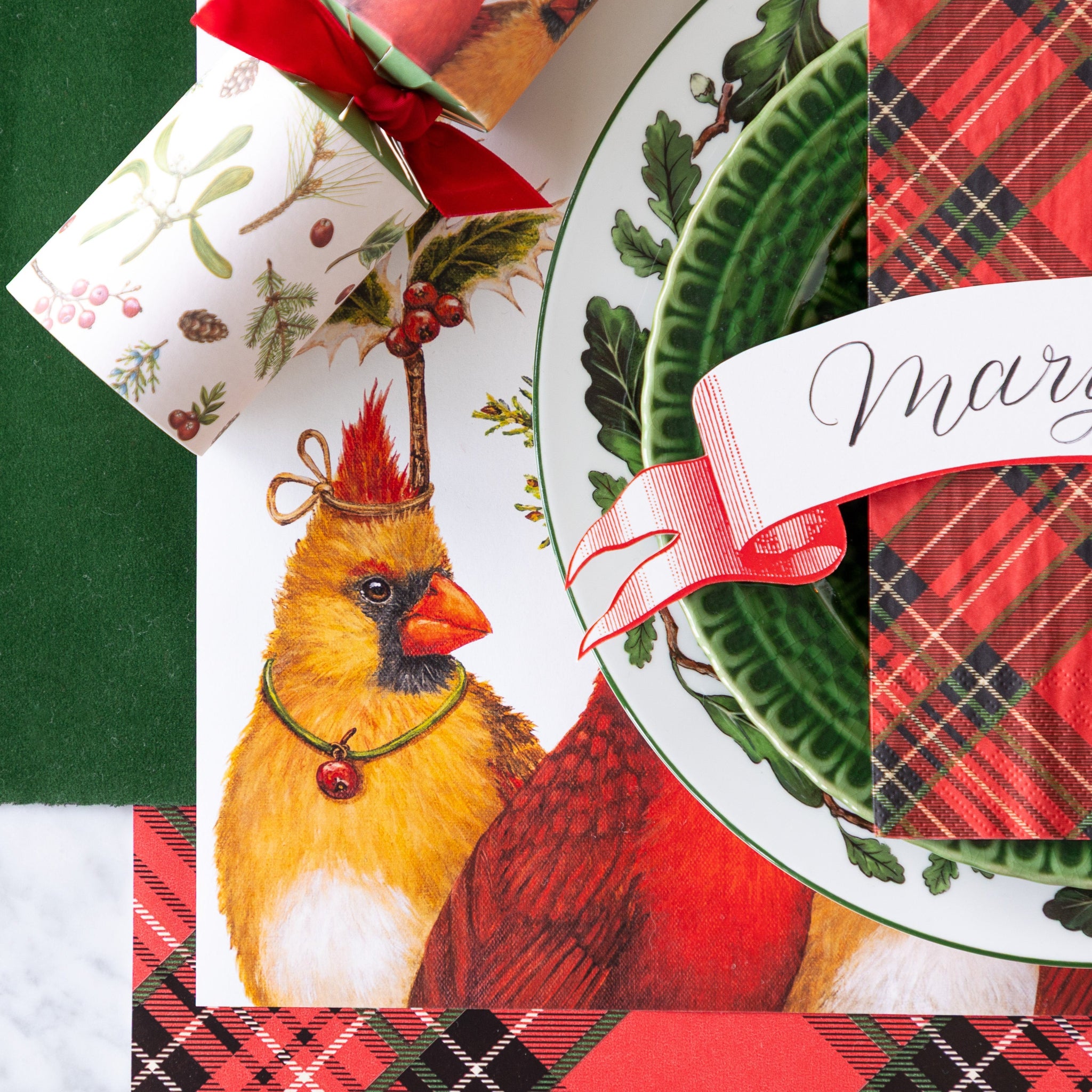 A festive place setting featuring the Cardinal Party Placemat with vintage dinnerware, Red Plaid Guest Napkin and Red Classic Banner Table Accent atop, on the Red Plaid and Green Flocked Runner.