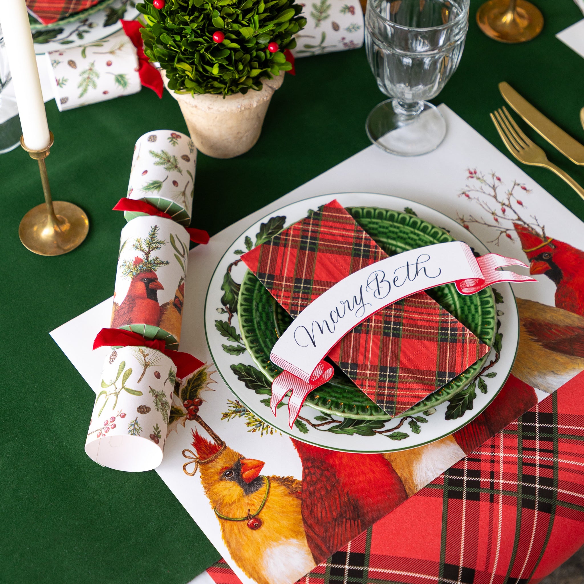 A festive place setting featuring the Cardinal Party Placemat, vintage dinnerware, Red Plaid Napkin, Red Classic Banner Table Accent and Cardinal Party Cracker atop.