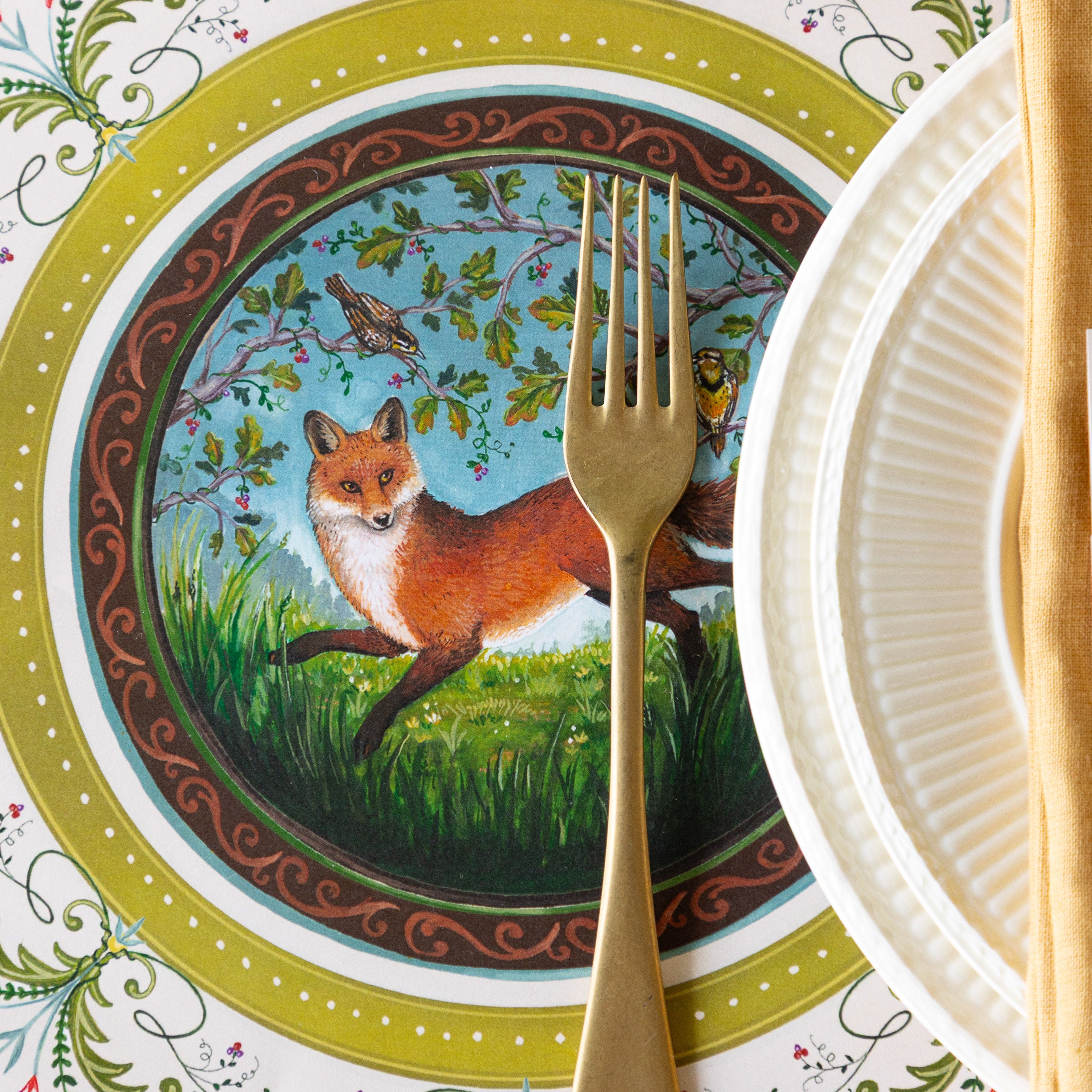 An elegant place setting with the Die-cut Fanciful Fox China Placemat offset under white dinnerware and a gold fork.