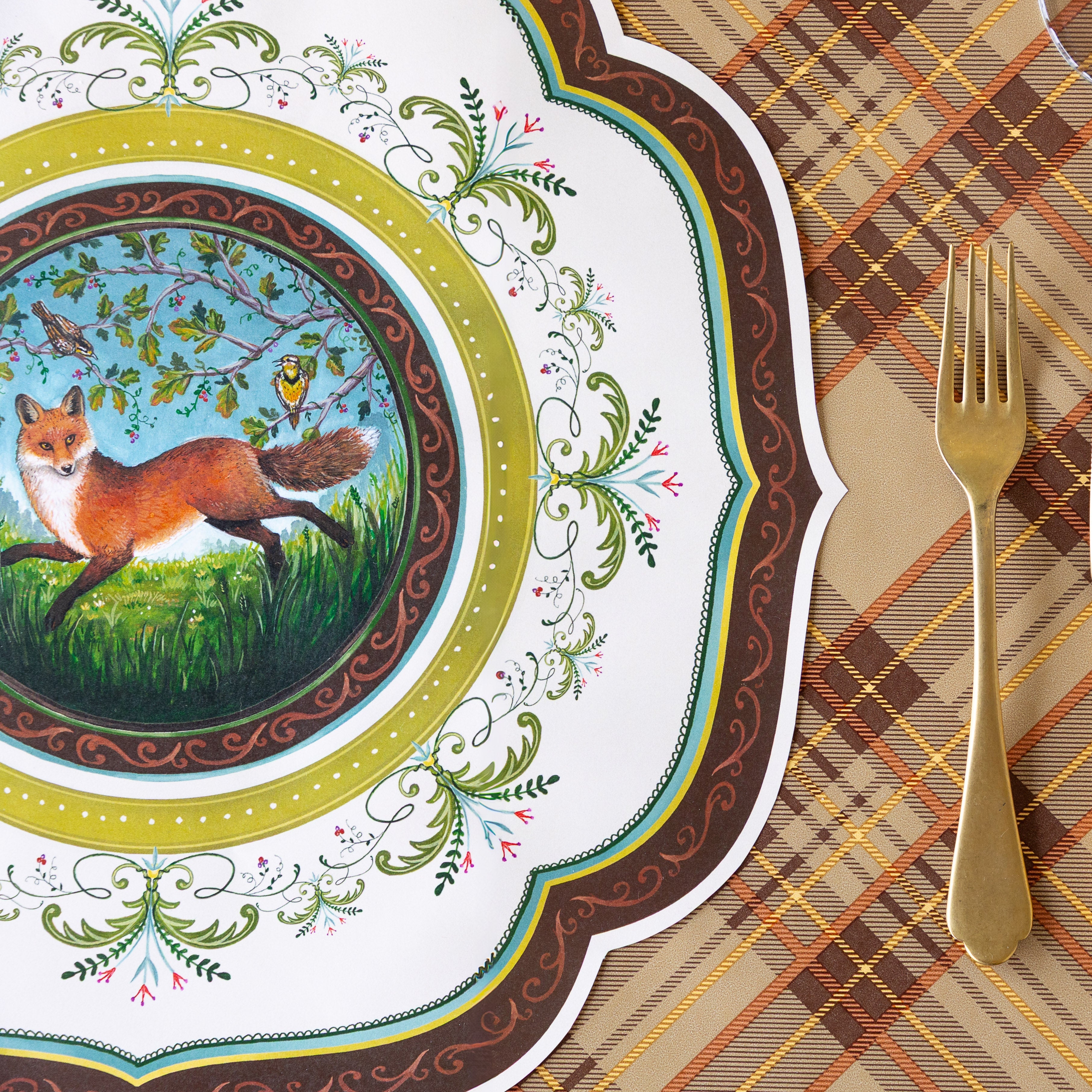 The Die-cut Fanciful Fox China Placemat next to a gold fork with the Autumn Plaid Runner underneath.