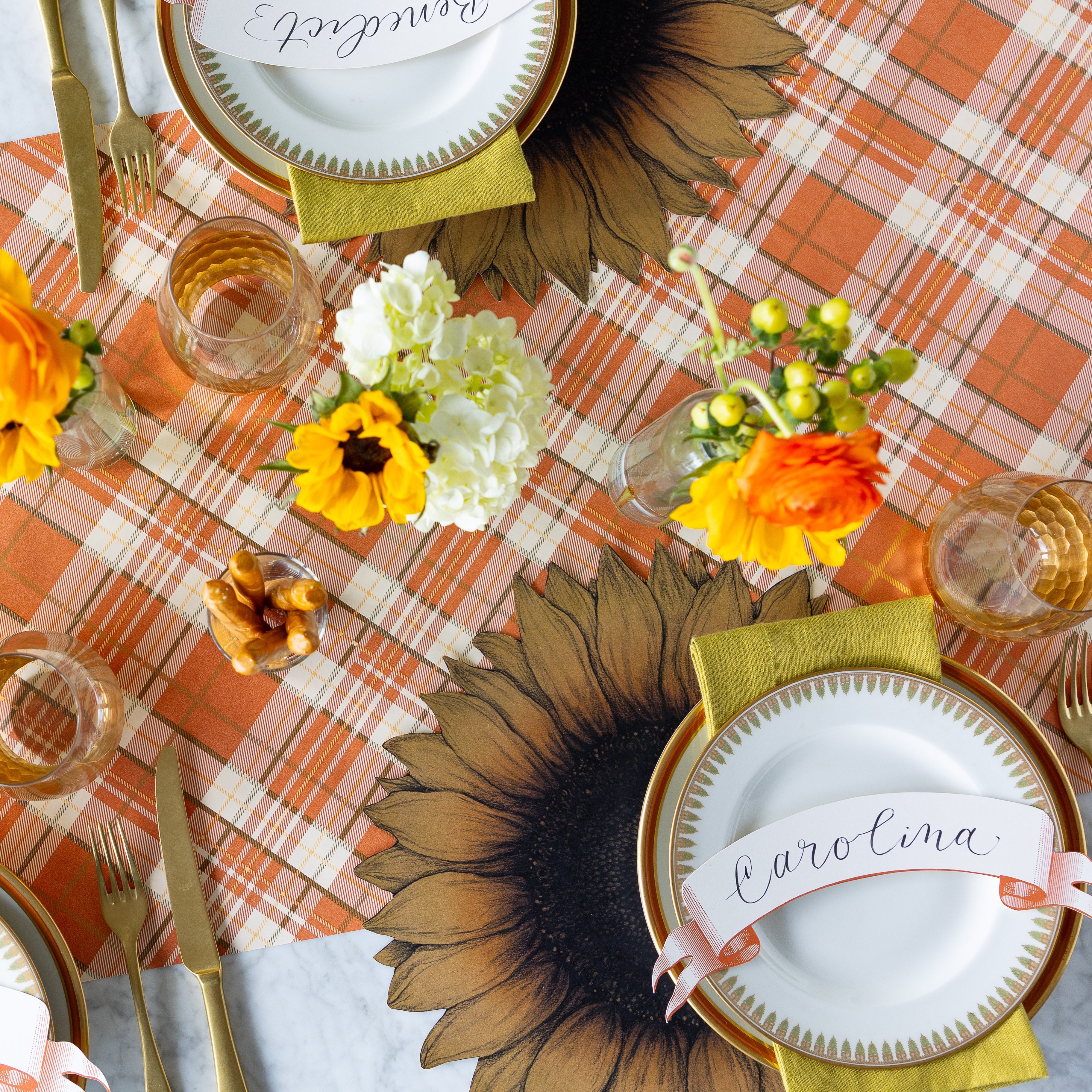 A charming table setting featuring the Die-cut Vintage Sunflower Placemat, gold-rimmed plate, green napkin, and a "Carolina" Orange Classic Banner Table Accent resting on the Autumn Plaid Runner.