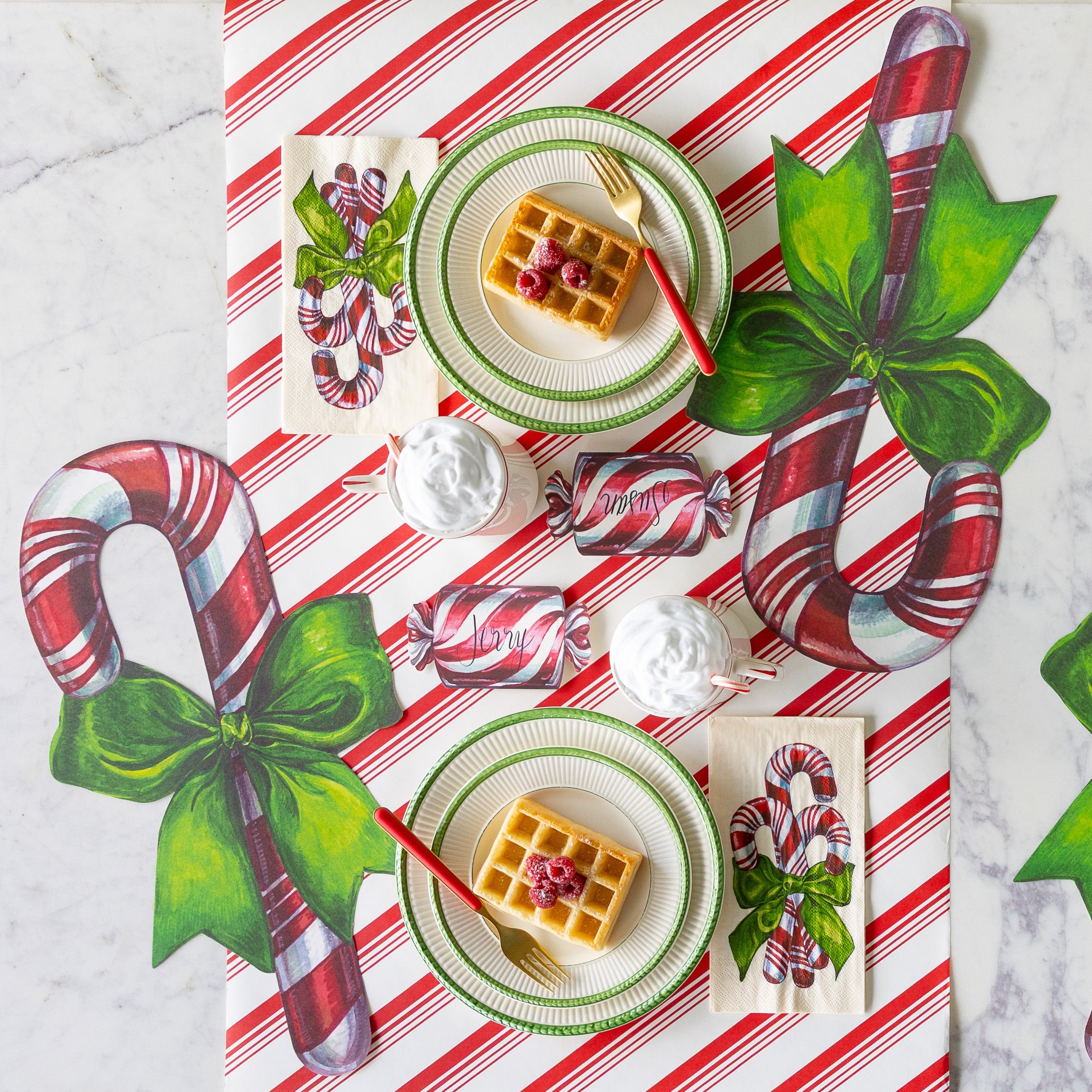 The Candy Stripe Runner under a table setting featuring the Die-cut Candy Cane Placemat, Candy Cane Guest Napkins, Christmas Candy Place Cards, plates with a waffle on them, and a cup topped with whip cream and a candy cane.